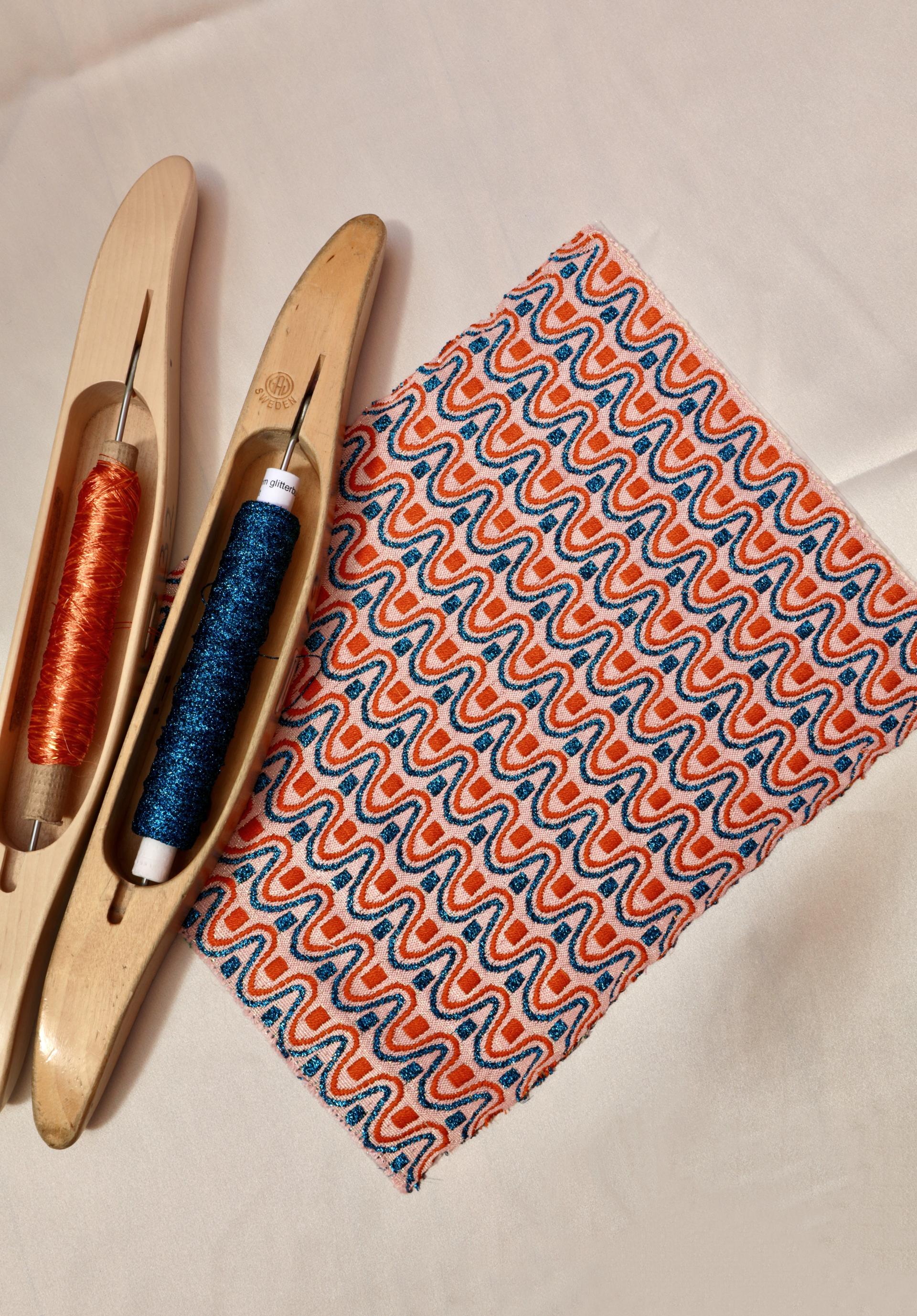 Colorful woven fabric featuring intricate wave patterns, accompanied by wooden weaving shuttles with vibrant threads.