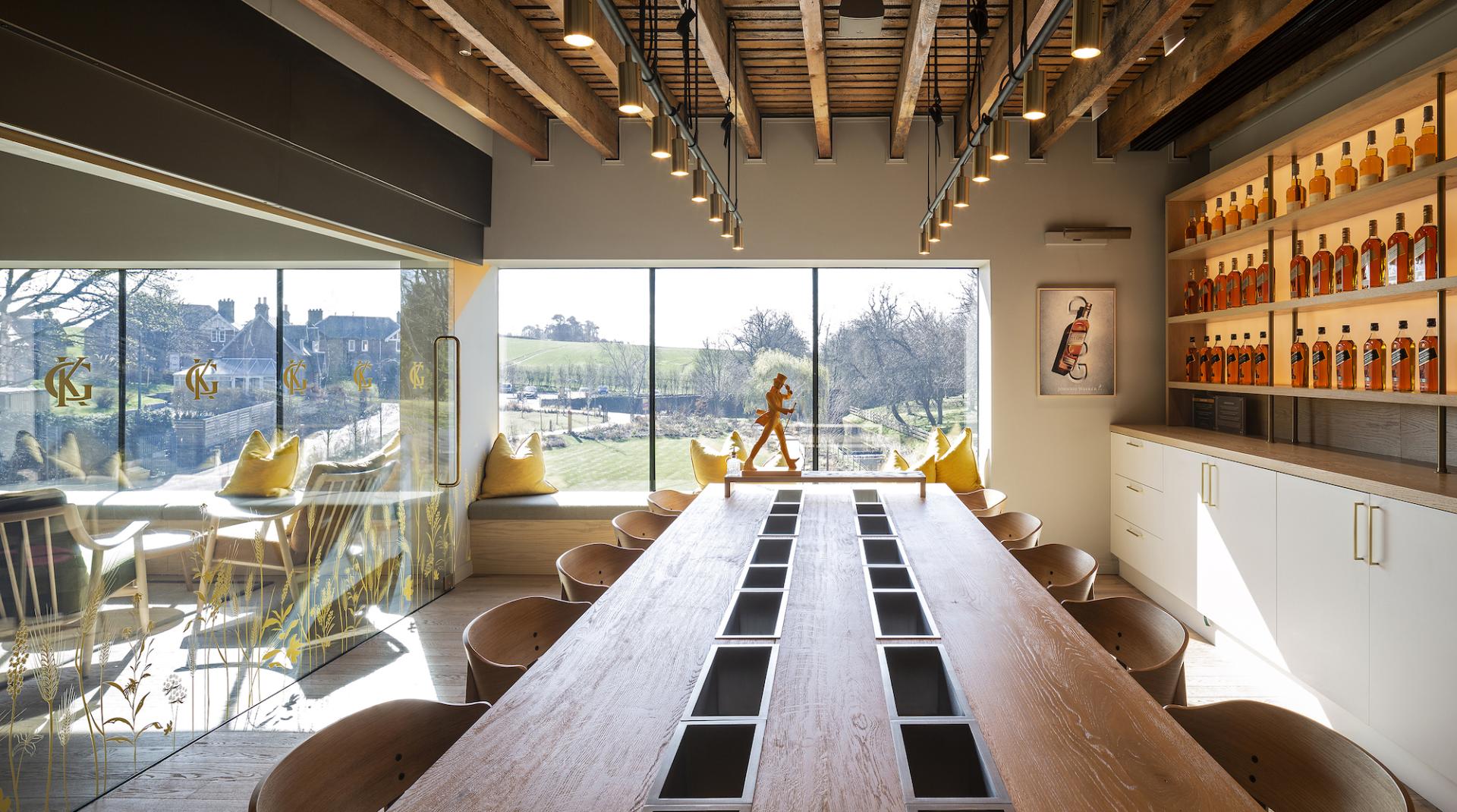 Bright, modern workspace featuring a long wooden table, whisky display, and large windows overlooking scenic landscapes.