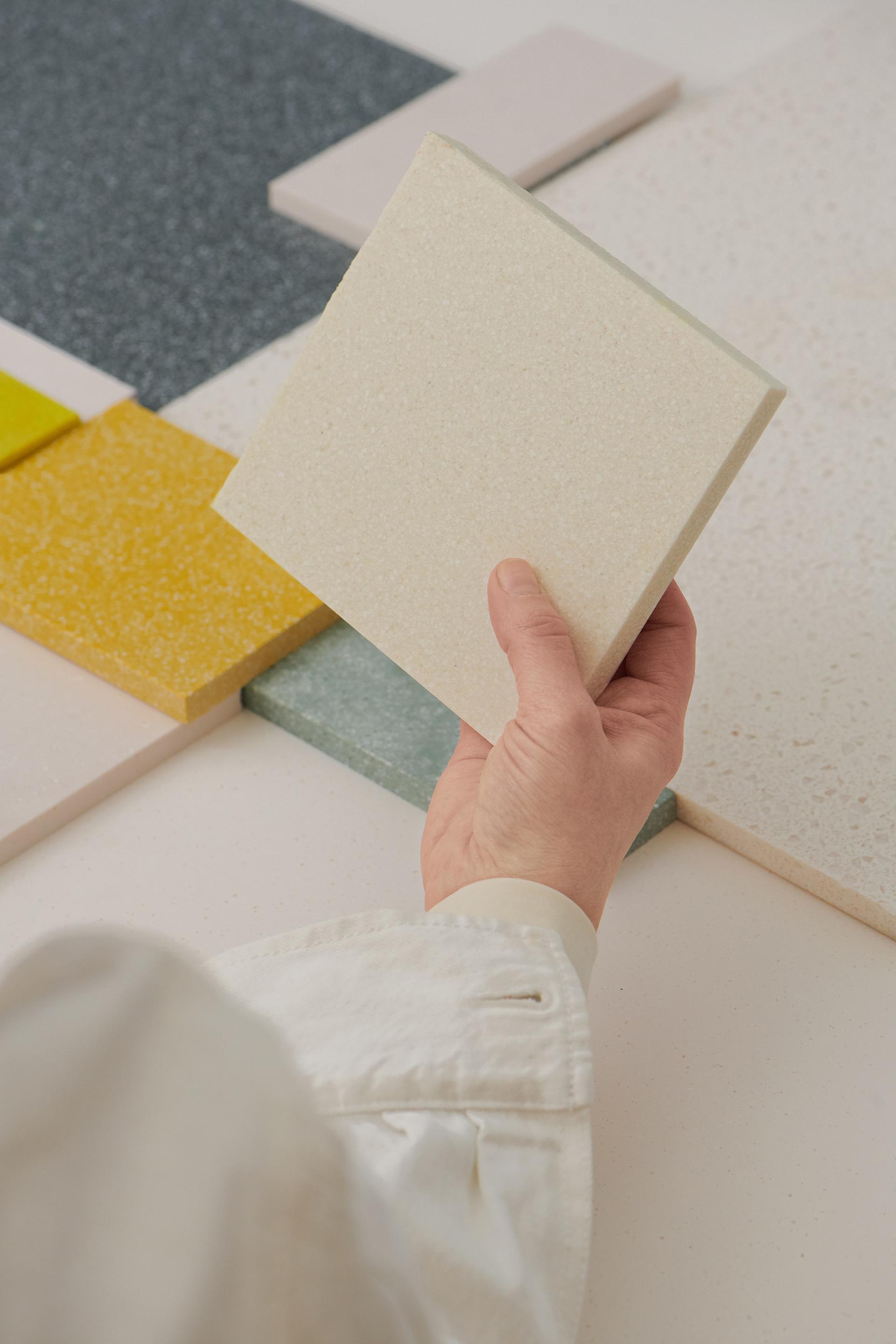 Hand holding a light-colored Durat Plus recycled surface sample among various colorful material samples.