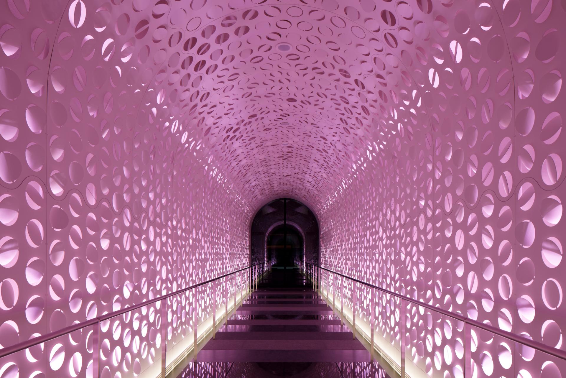 Illuminated hallway of W Osaka featuring circular cutouts and vibrant pink lighting, showcasing unique architectural design.