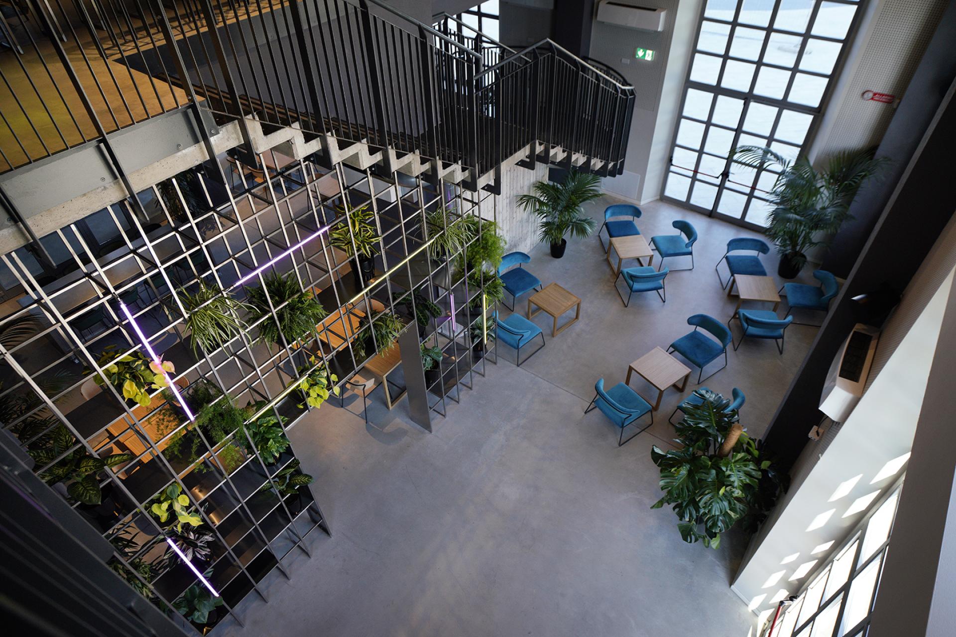 Modern interior of the former thermal power plant in Bergamo, featuring green plants and cozy seating areas.