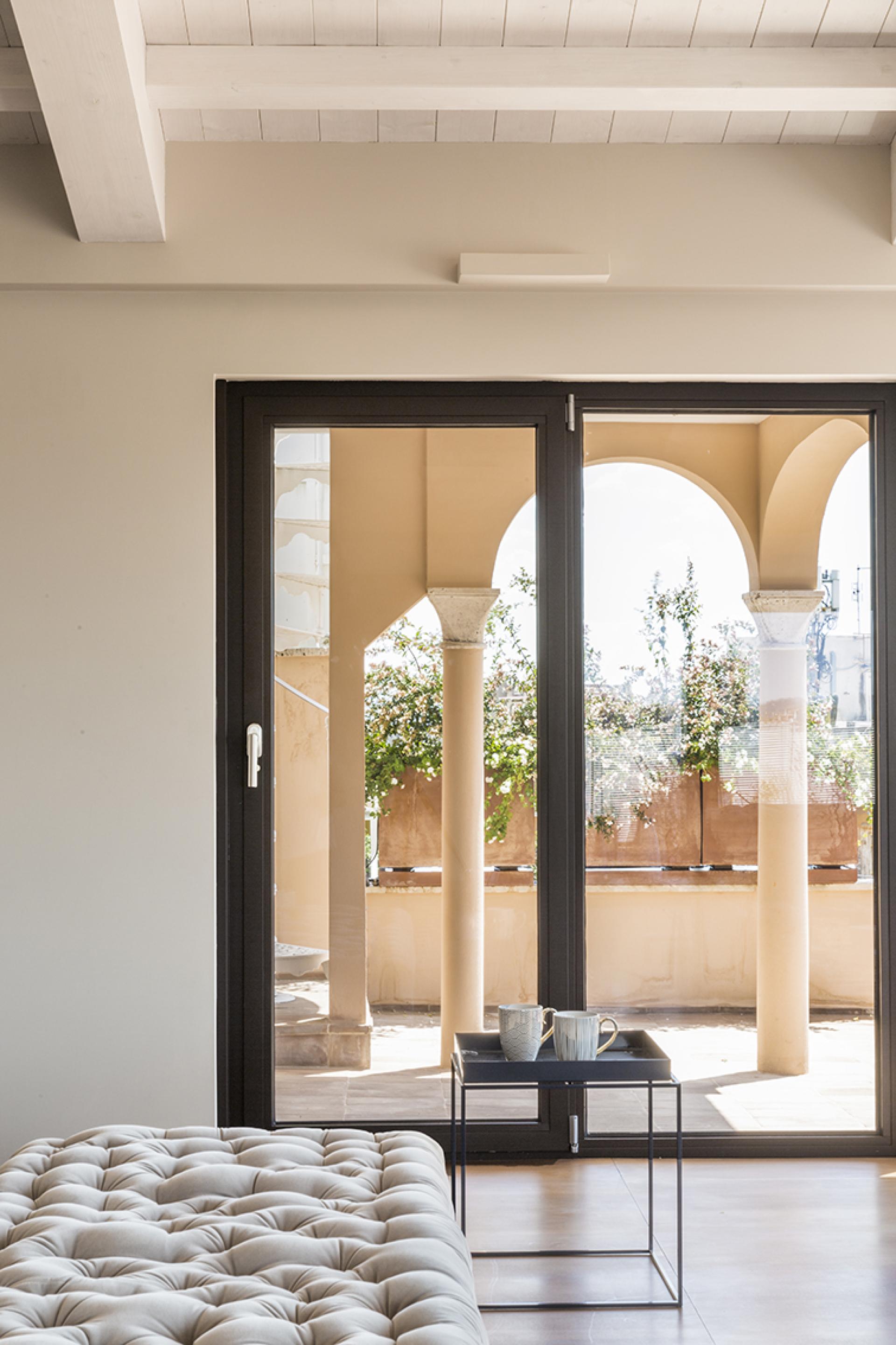 Brightly lit artist's loft interior featuring modern furnishings and arched windows overlooking a garden in Rome.