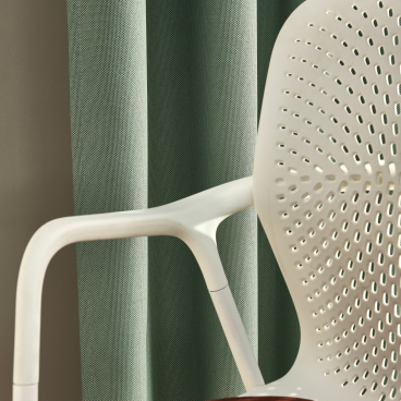 Recycled plastic textile curtains in green, paired with a modern chair featuring a red velvet seat, enhancing acoustic design.