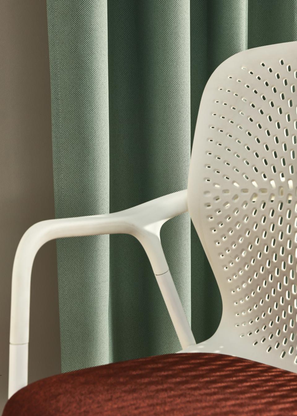 Recycled plastic textile curtains in green, paired with a modern chair featuring a red velvet seat, enhancing acoustic design.