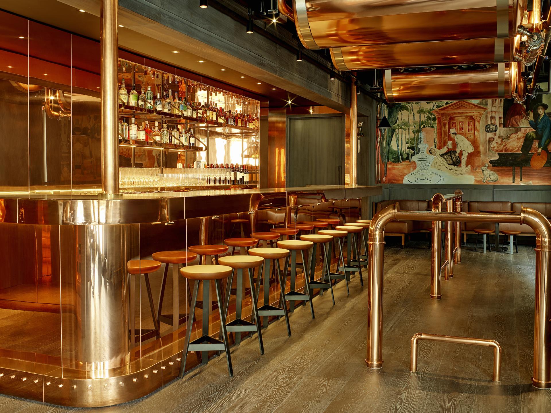 Stylish bar area at Leicester Square hotel features a copper design, modern seating, and a vibrant mural backdrop.