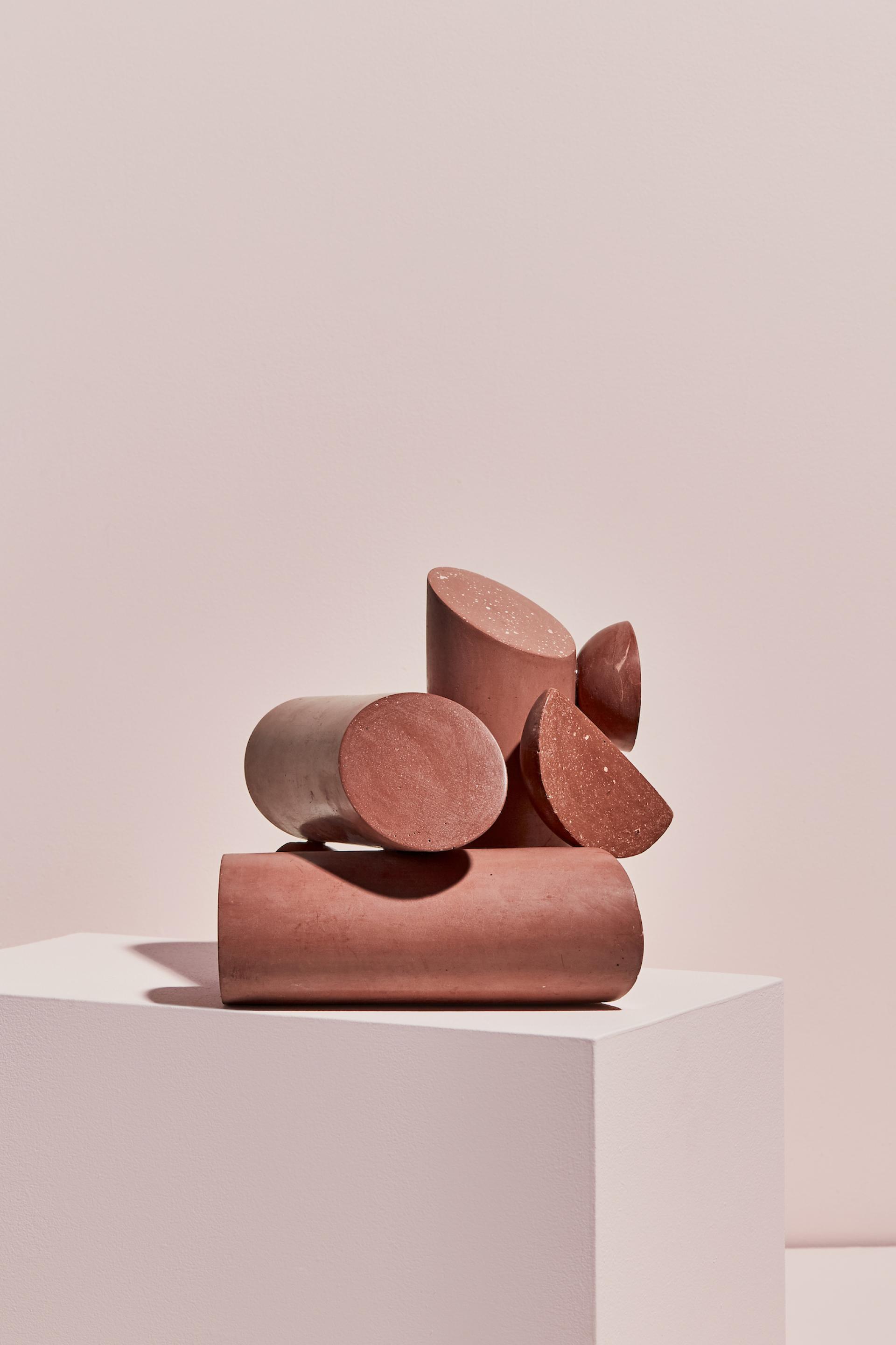 Sculptural forms made of clay in various shapes and shades of reddish-brown, displayed on a minimalist pedestal.