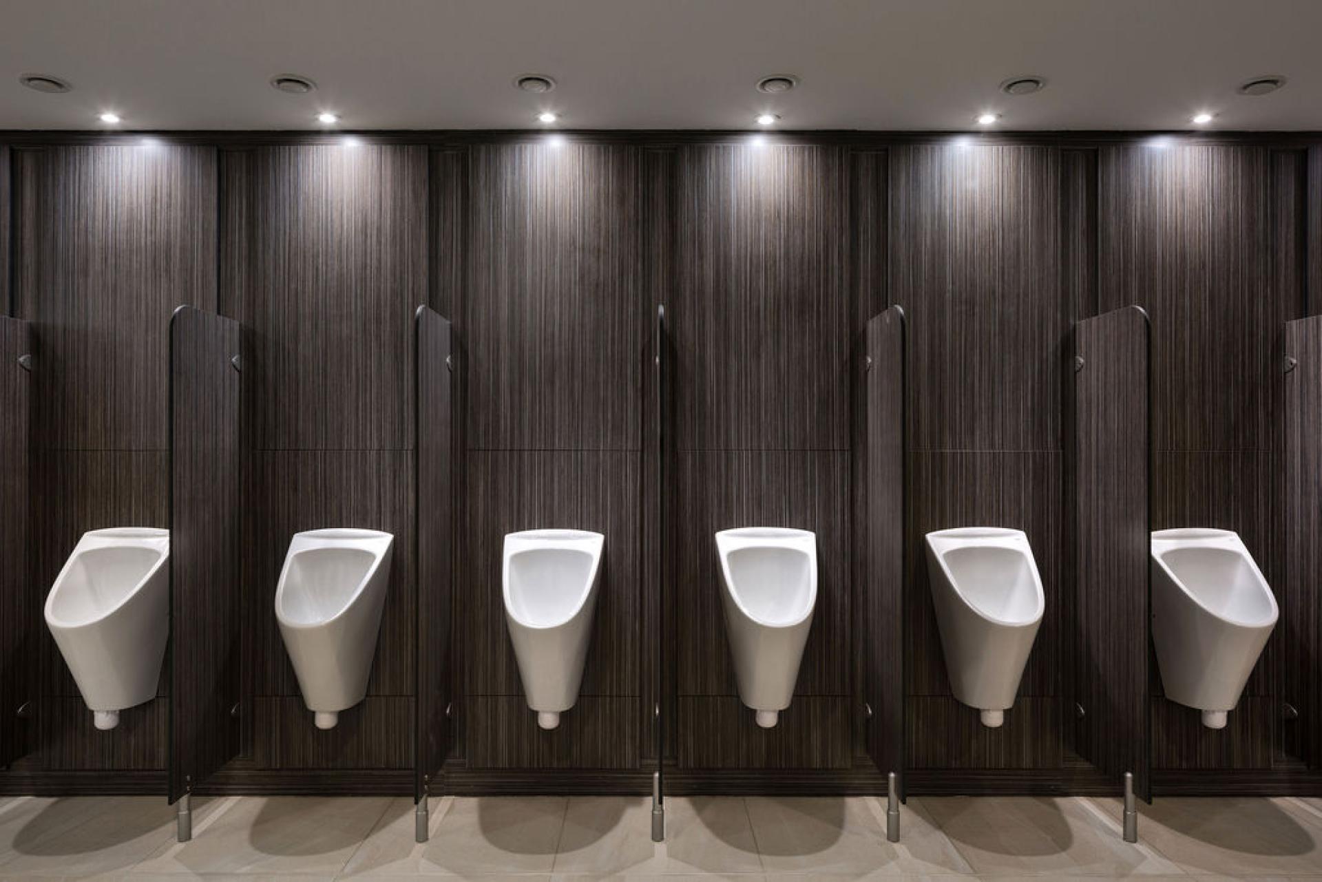 Modern washroom design featuring sleek white urinals against a dark wood-paneled wall, at Liverpool Street Station.
