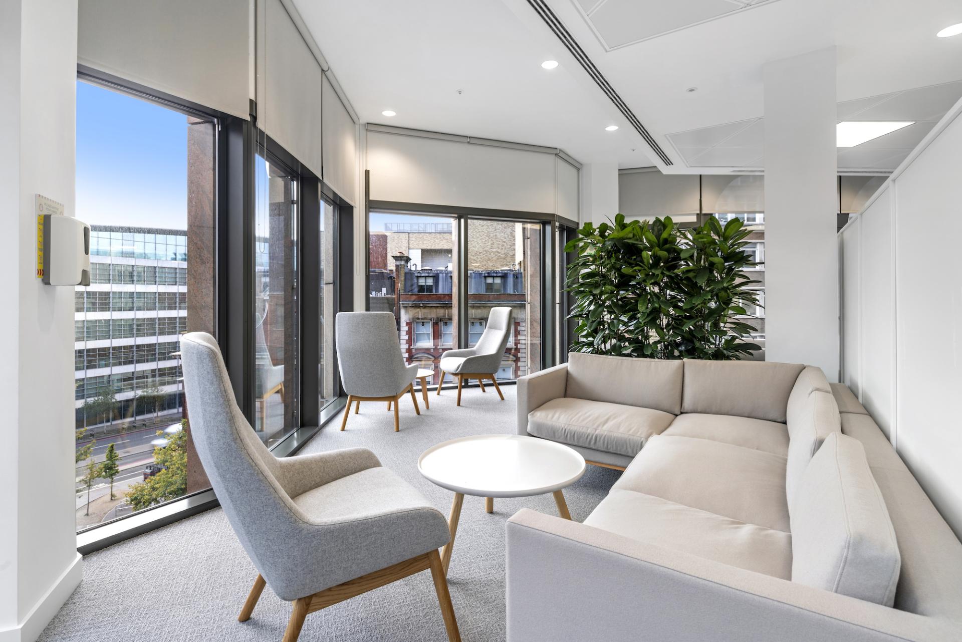 Contemporary office lounge featuring a sectional sofa, armchairs, and large windows with natural light and greenery.