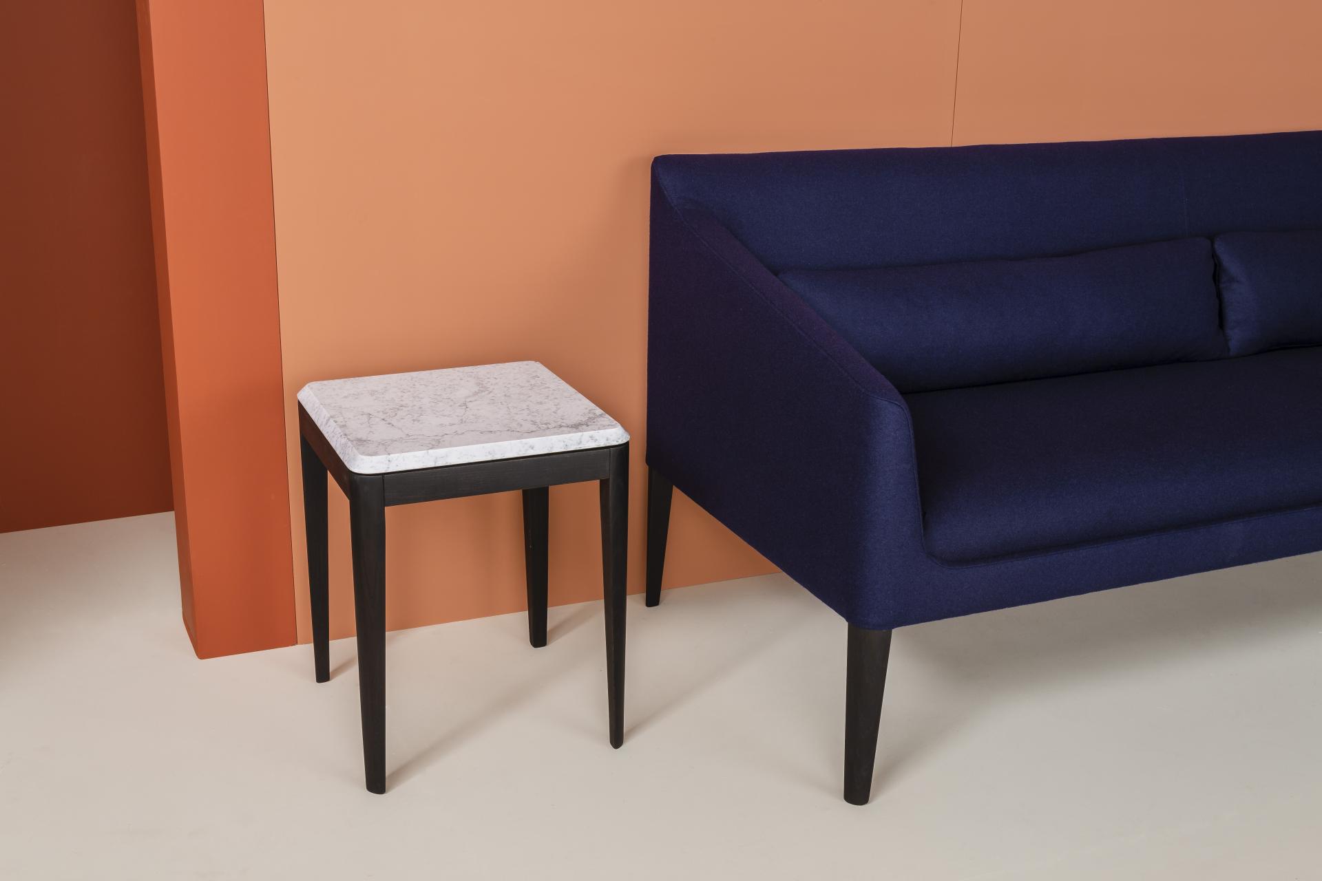Stylish navy sofa paired with a modern black-legged side table featuring a marble top against an orange backdrop.