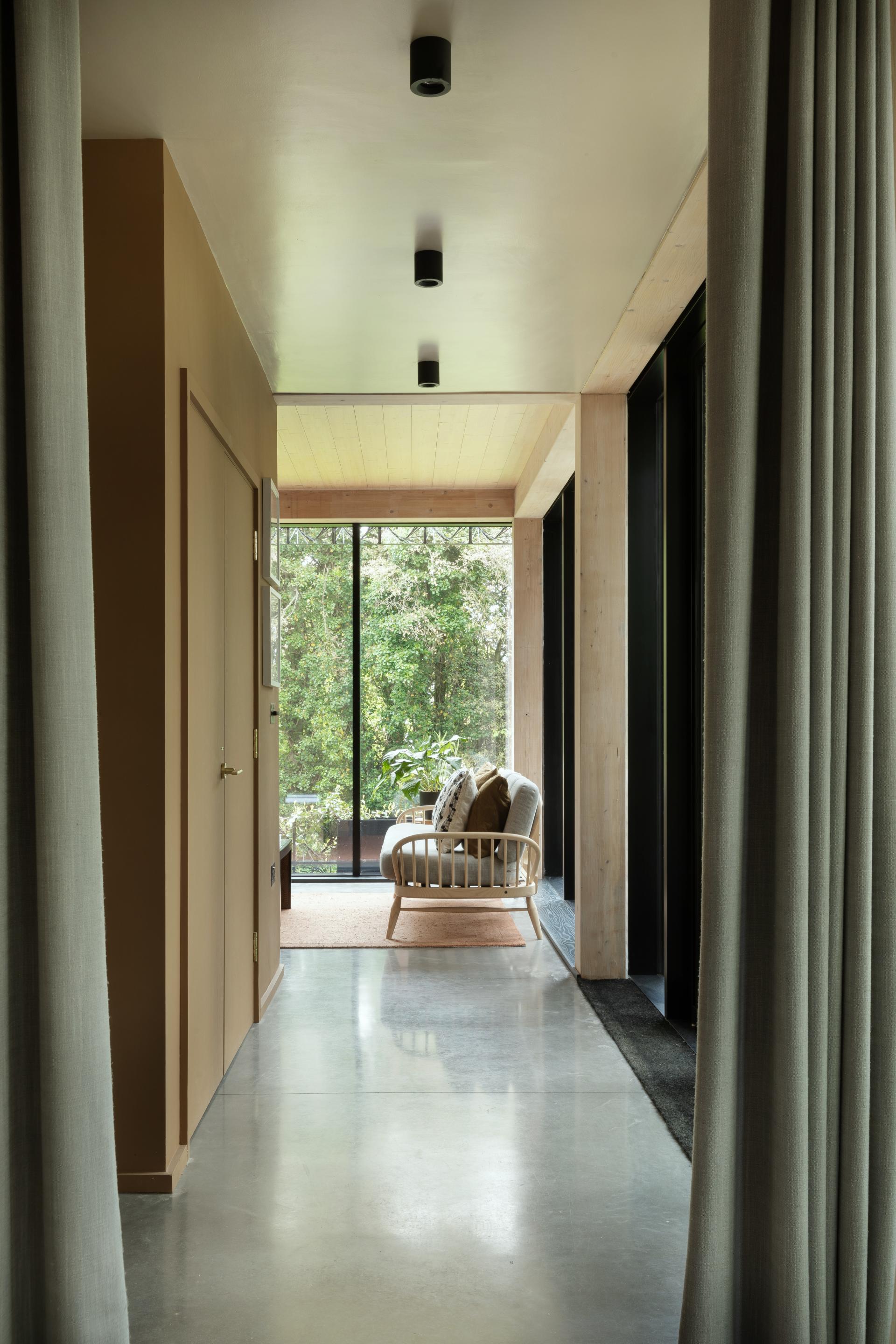Bright hallway leading to a cozy seating area, featuring large glass windows and natural greenery outside.