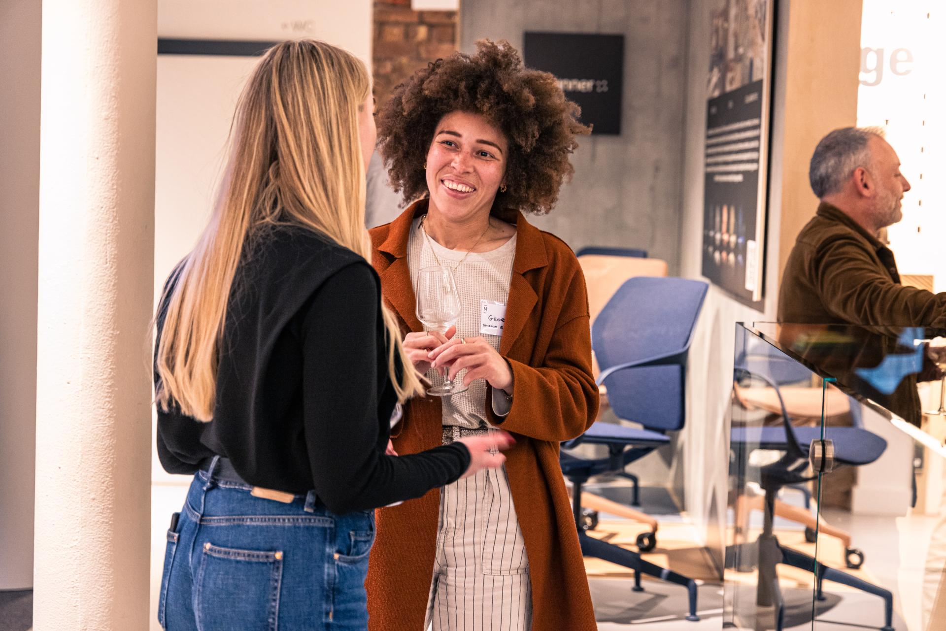 Two women engage in conversation at a Manchester property seminar, with modern furniture displayed in the background.
