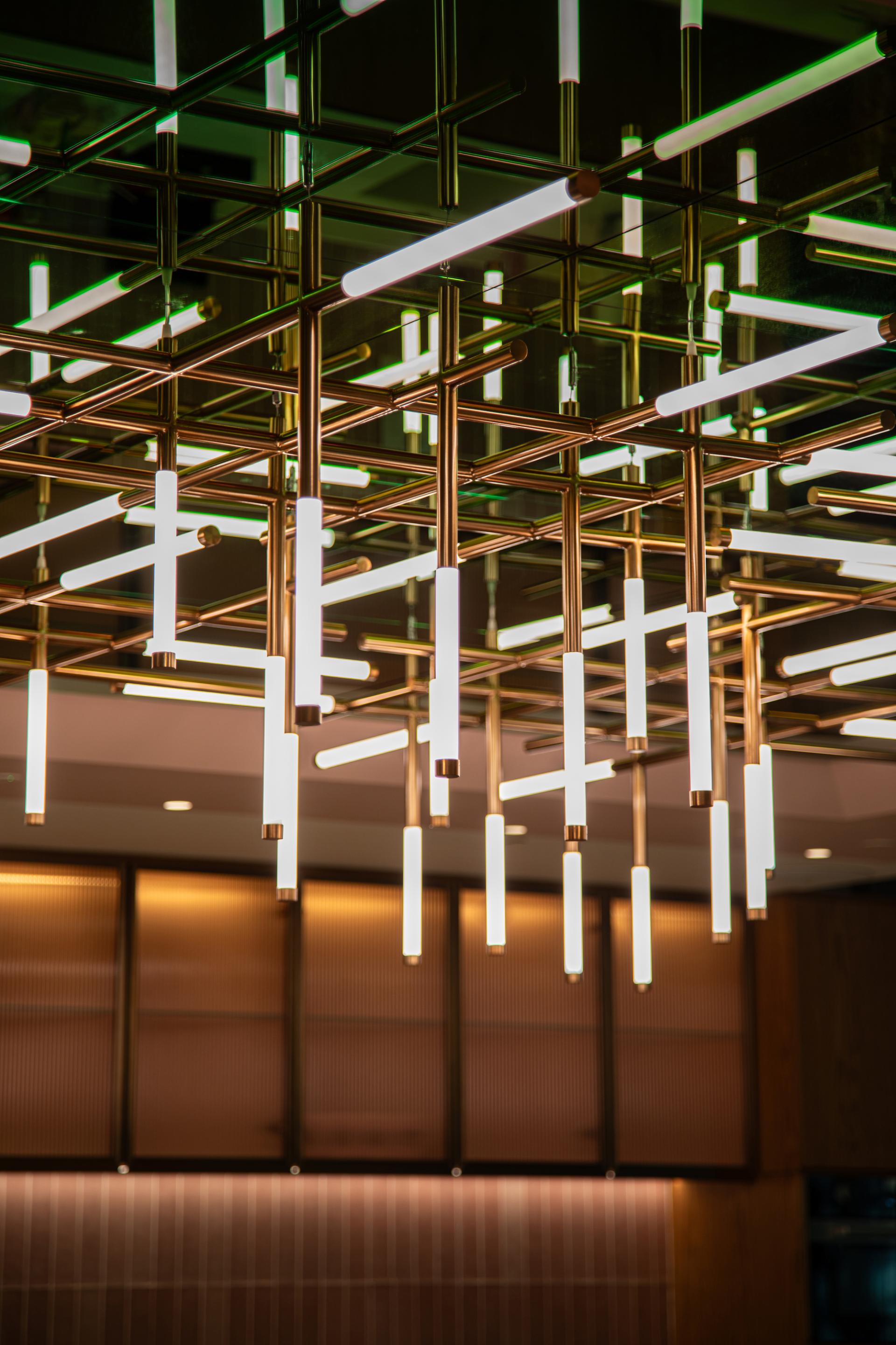 Modern chandelier installation with bright tubular lights, enhancing the vibrant atmosphere of a Dubai workplace inspired by nature.