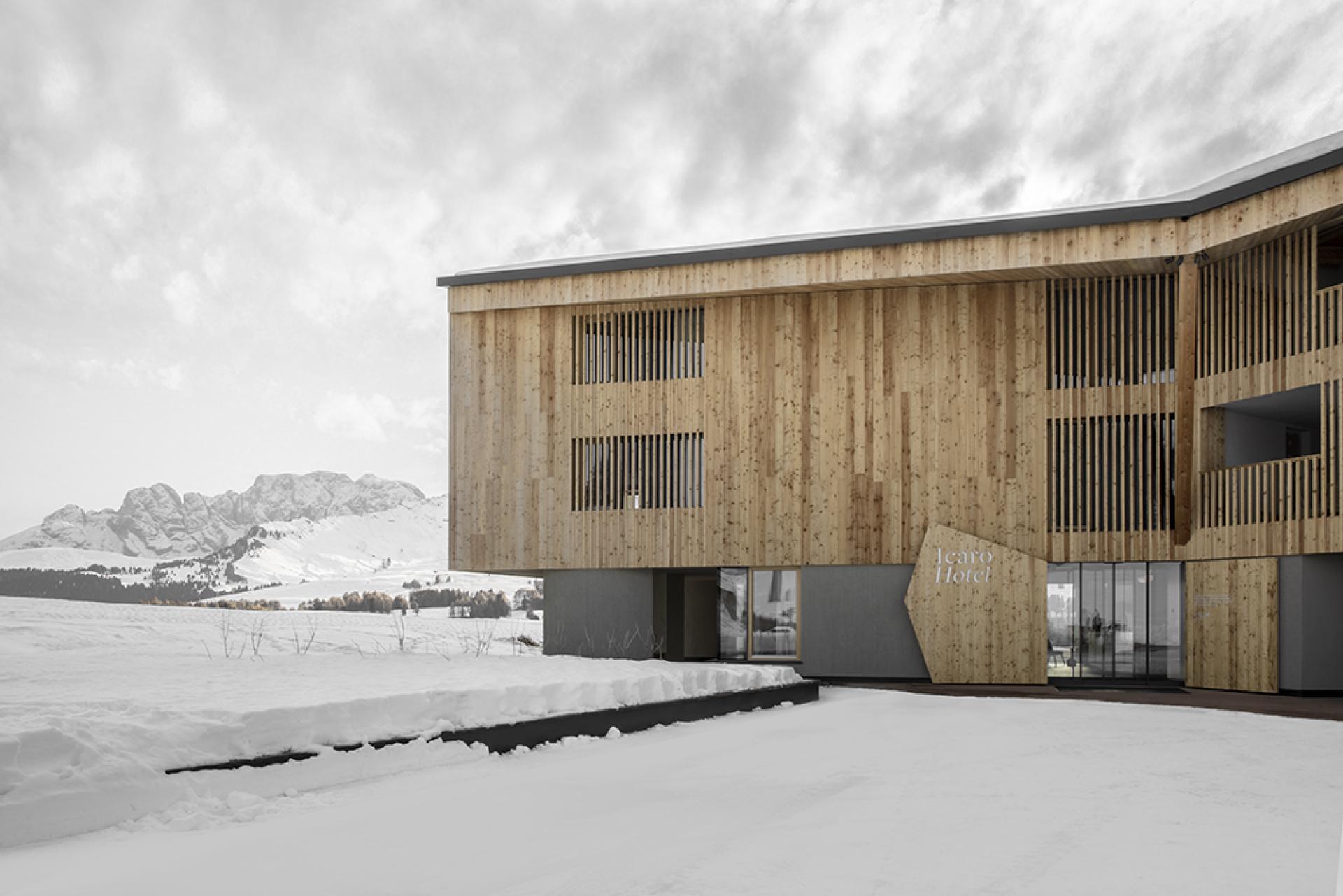 Modern wooden architecture of Icaro Hotel set against the snowy Dolomite Mountains, blending nature and design.