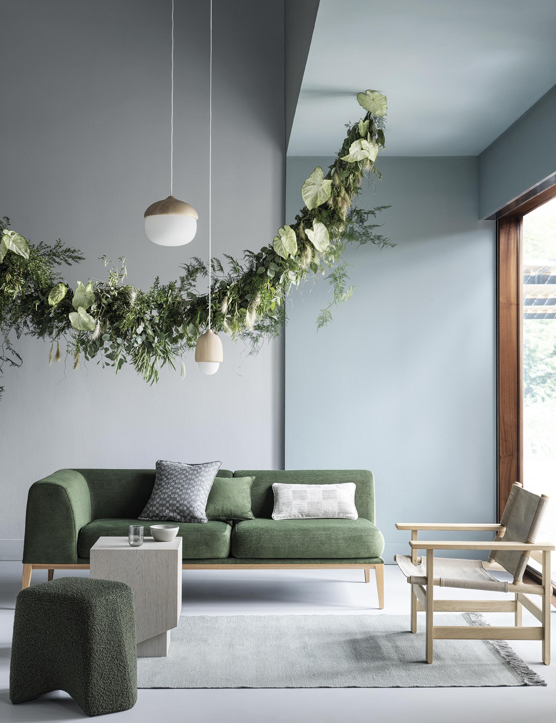 Stylish living room featuring a green sofa, natural light, botanical decorations, and calming SS22 color trends from Crown Paints.