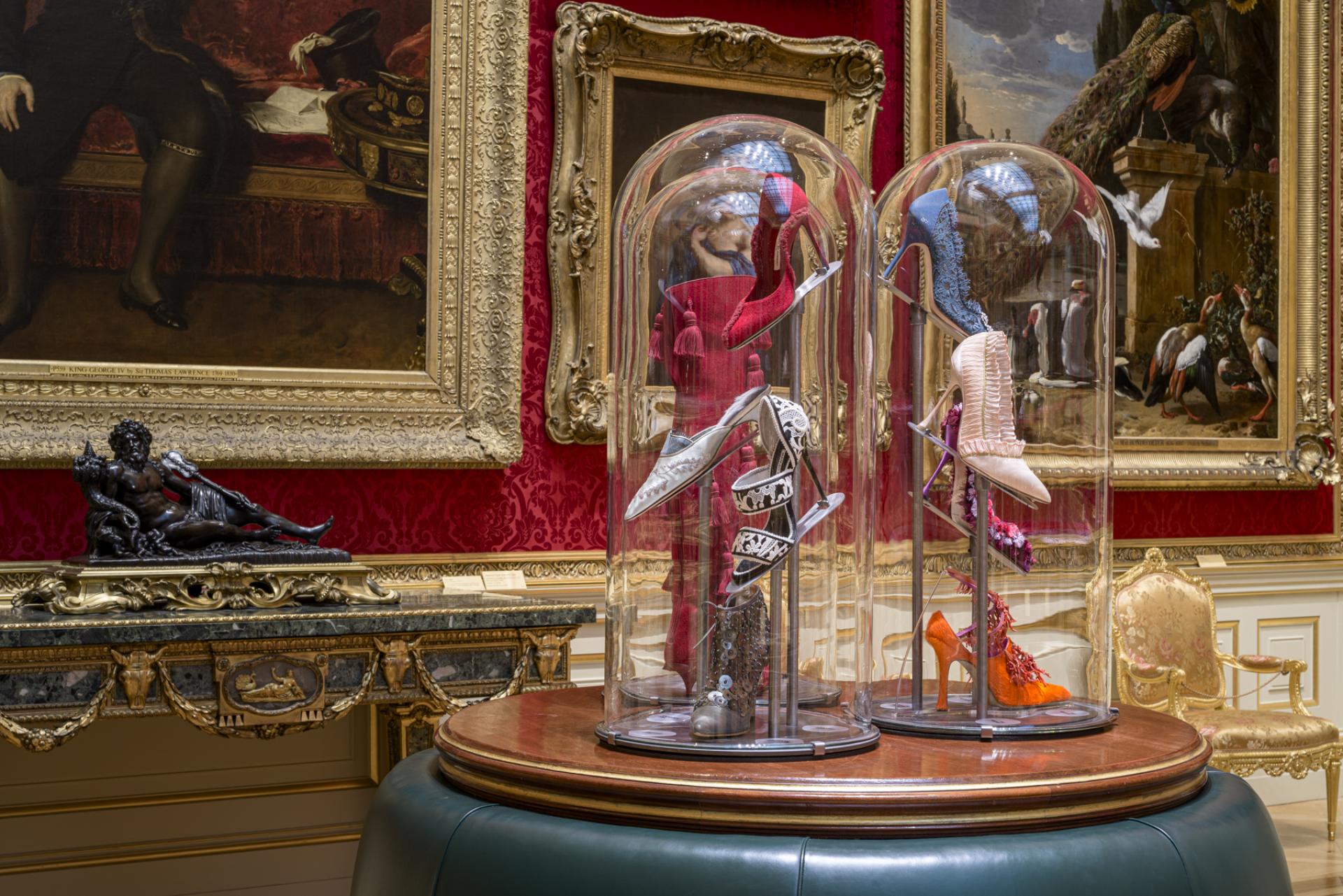 Exquisite designer shoes displayed in glass domes, set against richly decorated historical interiors.