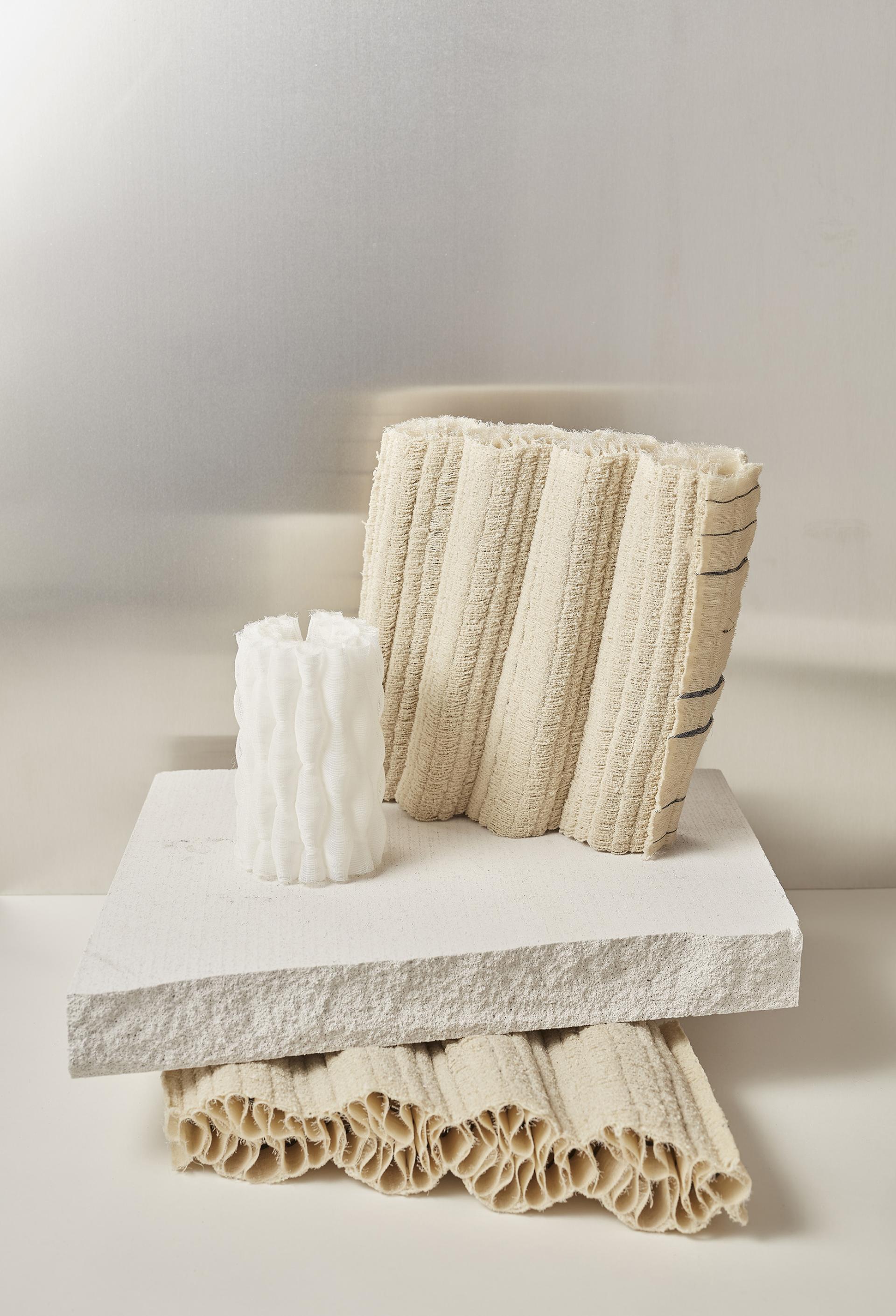 Textured fabric samples and a sculptural candle displayed on overlapping white surfaces, showcasing Heimtextil’s innovative design trends for 2021/22.