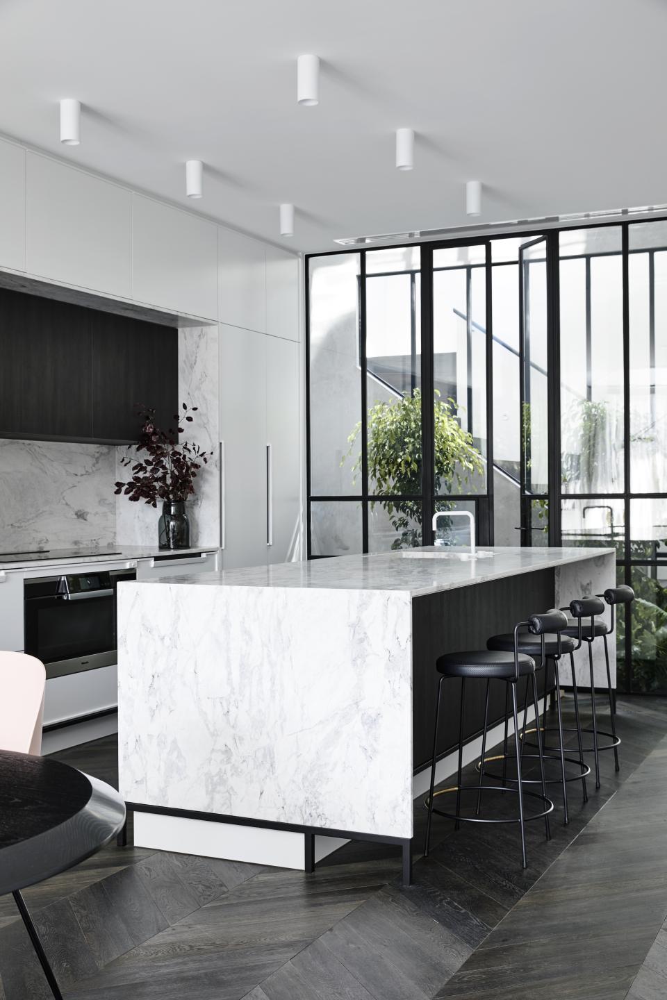 Modern kitchen featuring a marble island, black stools, and large windows, inspired by Parisian design in a Melbourne home.