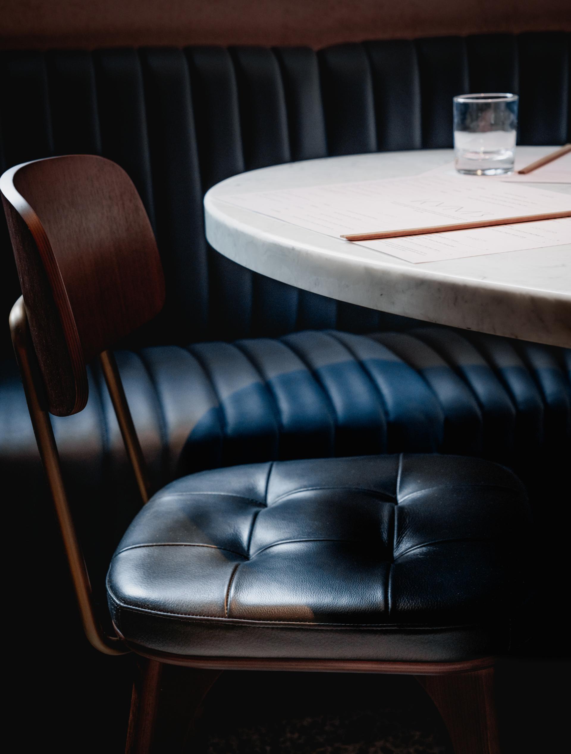 Stylish black leather chair beside a round marble table in Andrew Wong's new restaurant design at Bloomberg Arcade.
