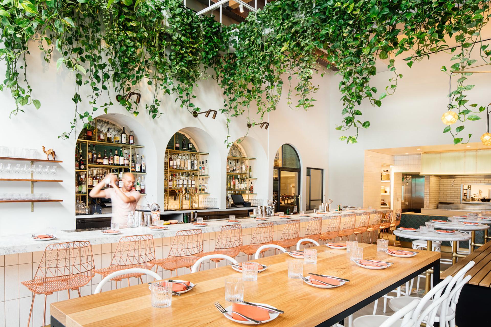 Stylish restaurant interior featuring vibrant greenery, a chic bar, and modern dining setup by Studio Unltd for Bavel.