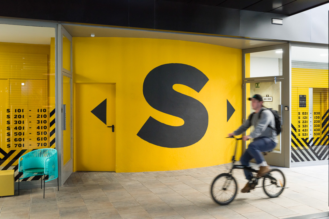 Vibrant interior of The Student Hotel Barcelona featuring a cyclist, bold yellow walls, and contemporary design elements.