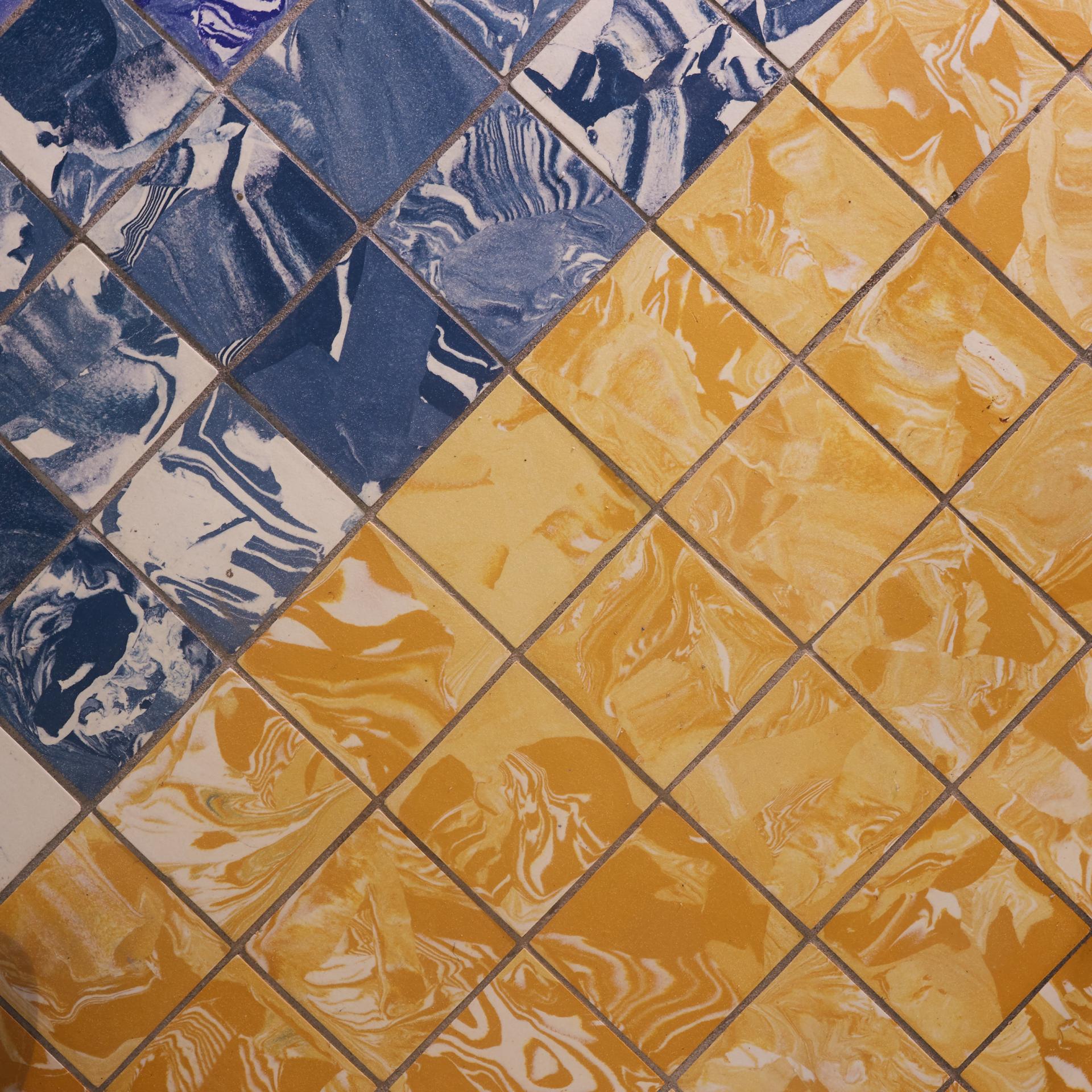 Vibrant encaustic tiles featuring blue marbled patterns and warm yellow hues from Granby Workshop's collaboration with Pentagon Tiles.