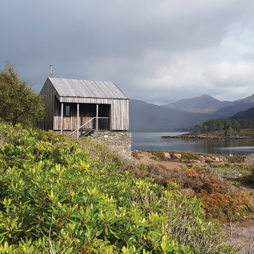 Wooden cabin near a serene Scottish loch, surrounded by lush greenery and mountains, reflecting Michele Bianco's outdoor inspiration.
