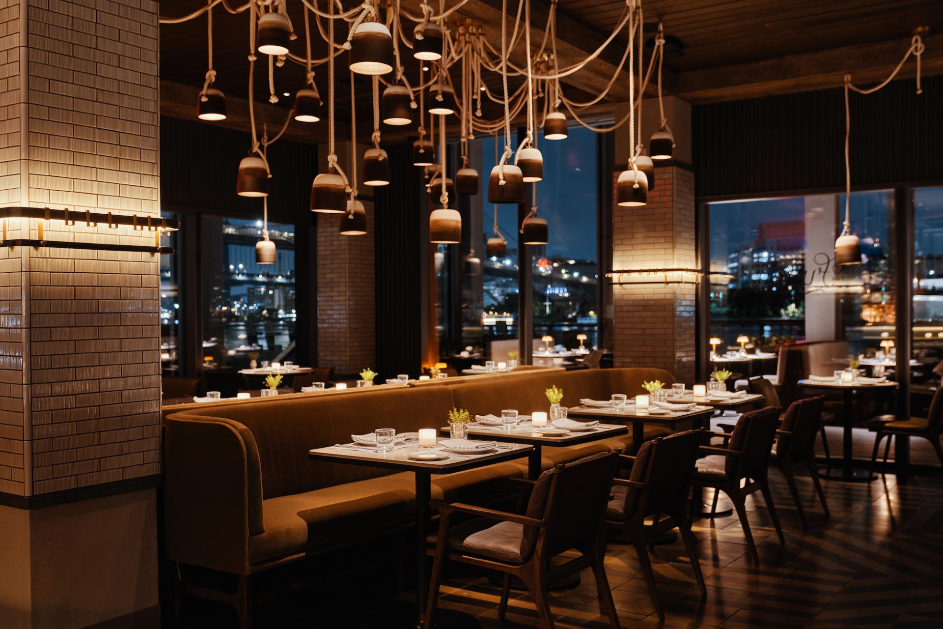 Elegant restaurant interior designed by Yabu Pushelberg, featuring cozy seating, ambient lighting, and urban views at night.