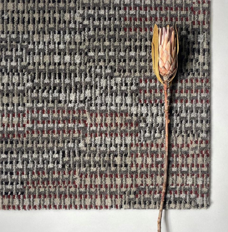 Textured carpet in natural tones with a dried flower, illustrating sustainable design and eco-friendly materials in interiors.