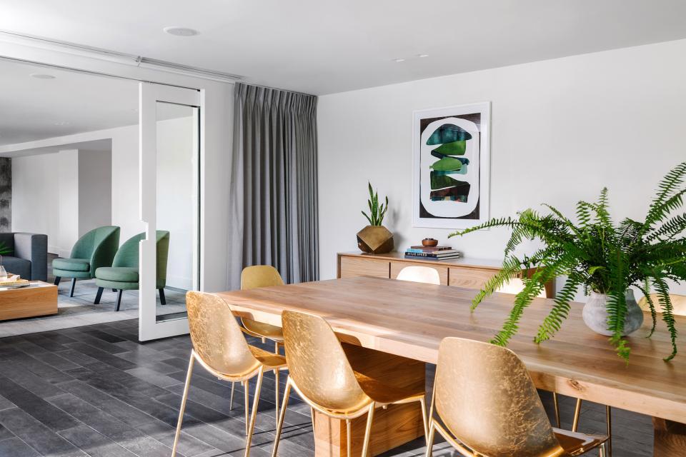 Stylish dining area featuring a wooden table, gold chairs, green accents, and contemporary art in a mid-century hotel.