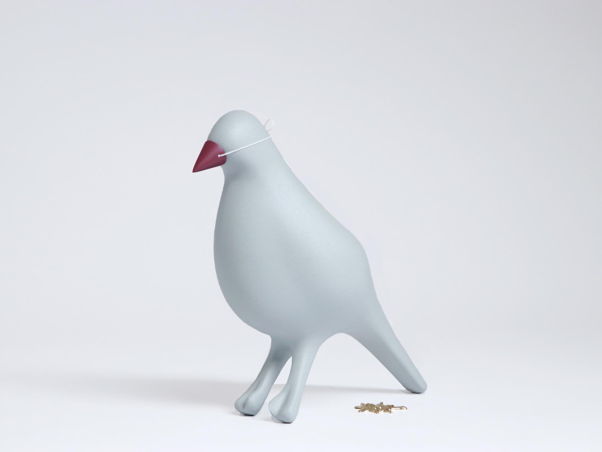 Stylized gray bird sculpture with a red beak, representing innovative design in material experimentation by May Wild Studio.