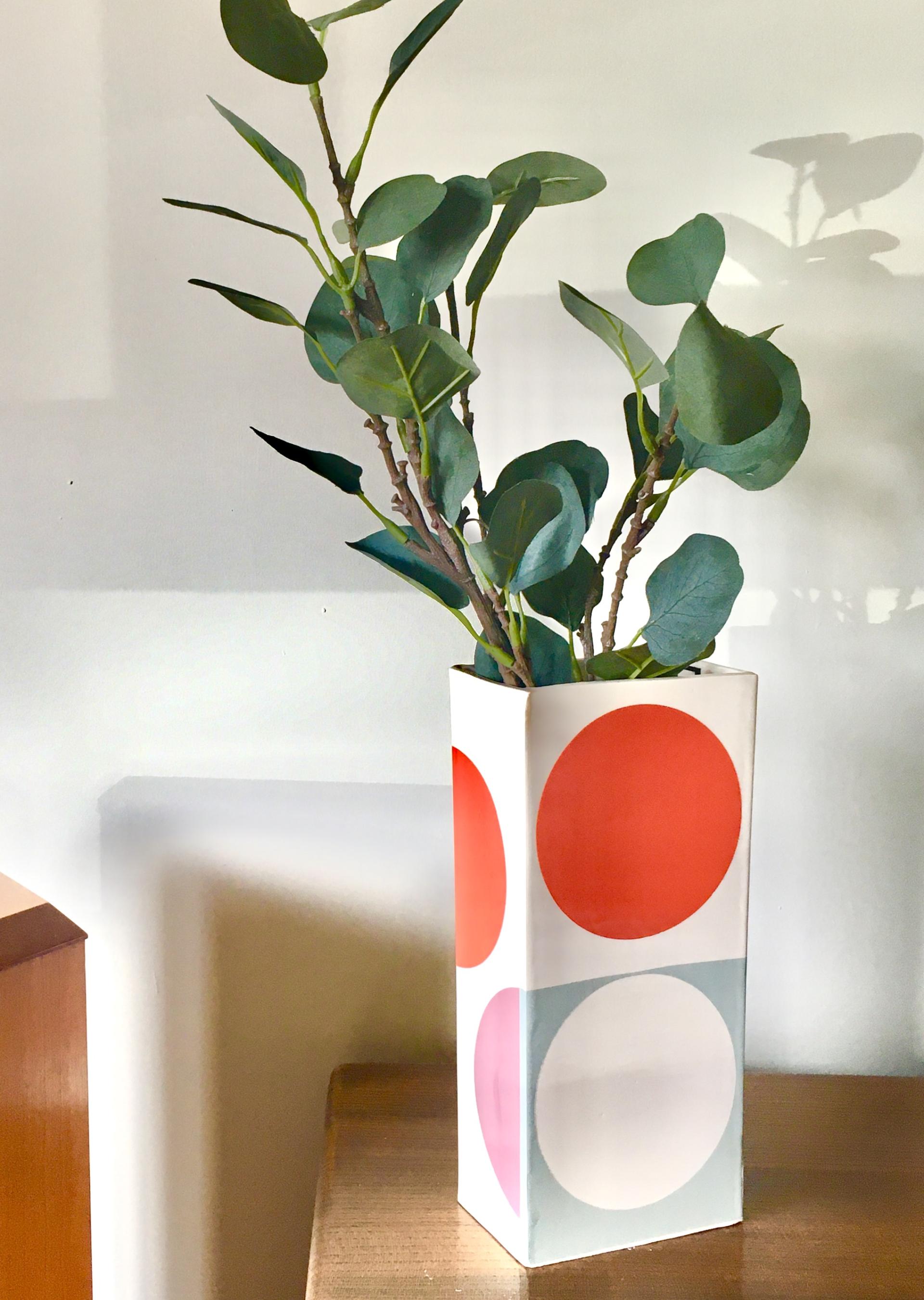 Colourful ceramic vase featuring bold geometric patterns, holding lush green foliage, showcasing Laura Lightbody's artistic craftsmanship.