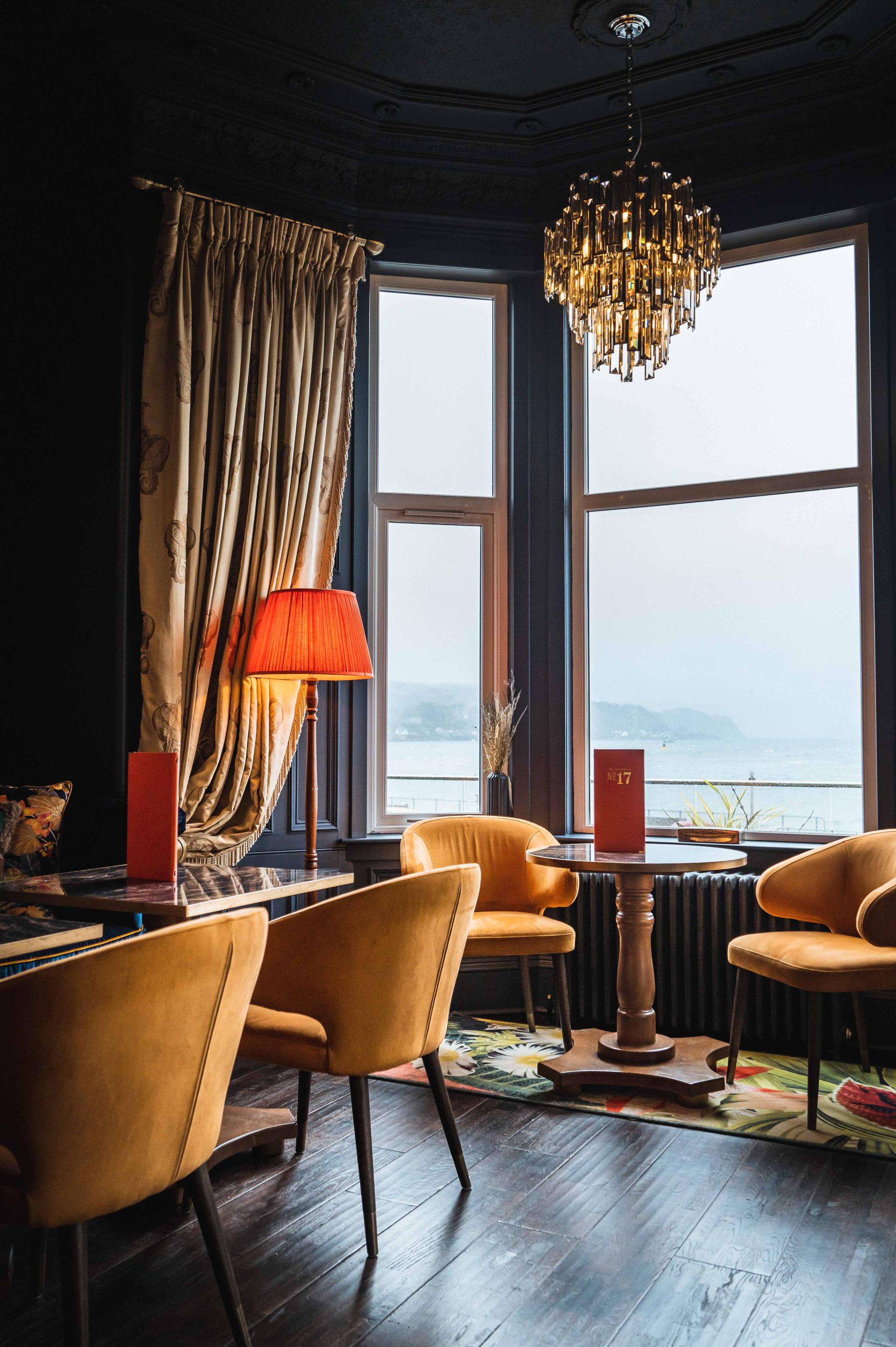 Elegant interior of No. 17 The Promenade Hotel in Oban featuring stylish seating, chandelier, and scenic window view.