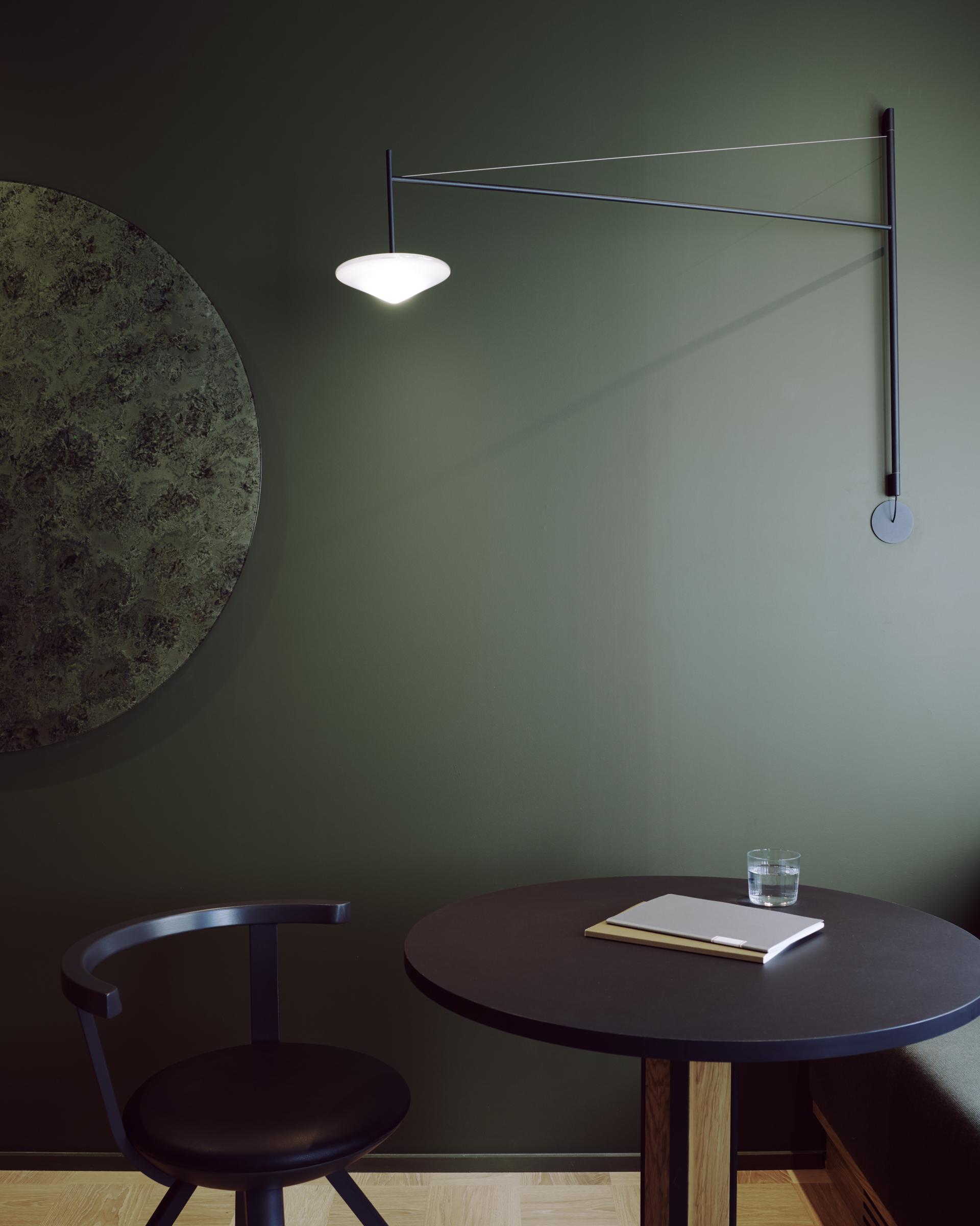 Stylish workspace featuring a black table, leather chair, and minimalist wall lamp in a soothing green environment.