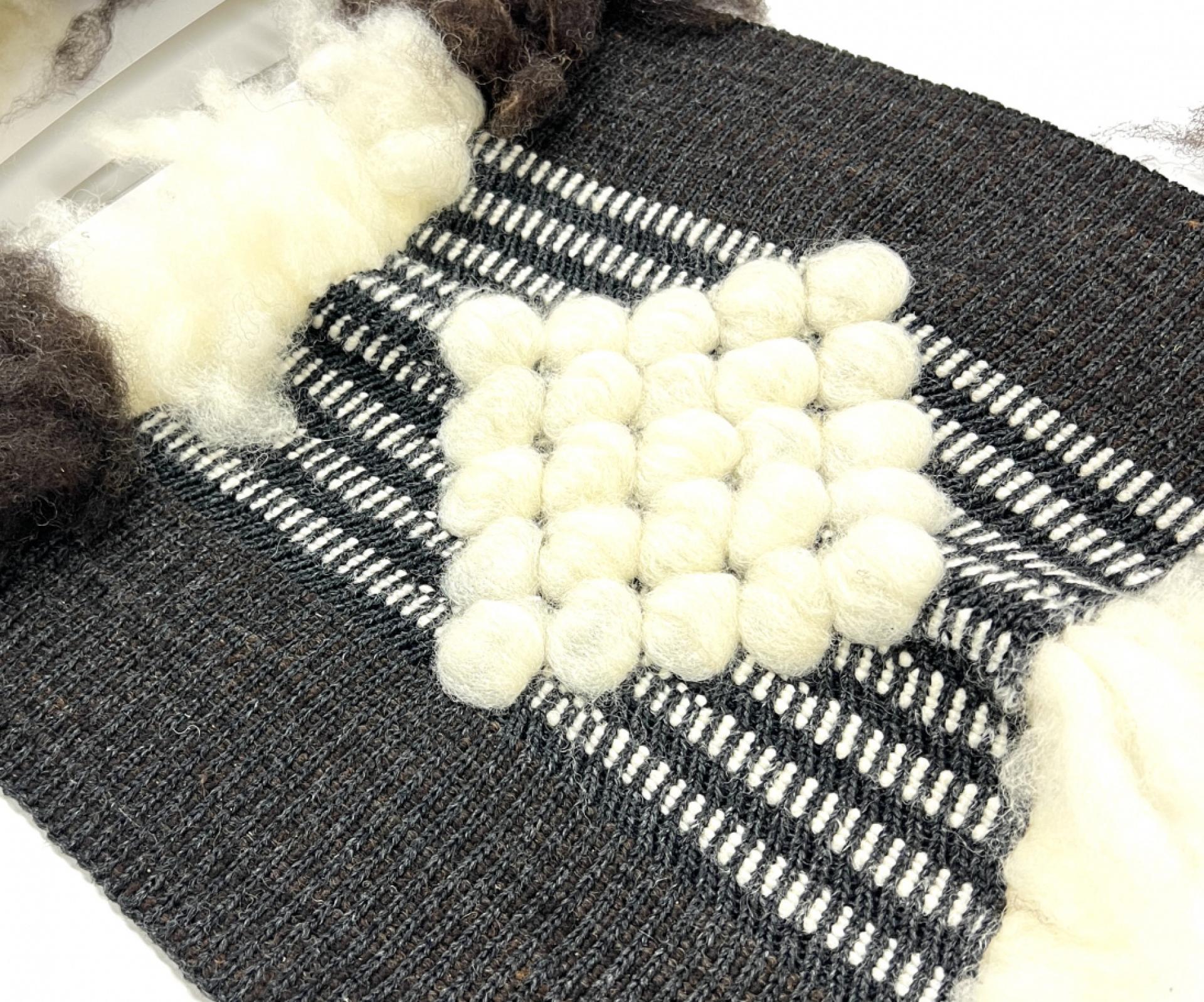 Textile artwork showcasing a textured weaving with black and white patterns, featuring fluffy white and brown fibers, from Graduate Design Show 2023.