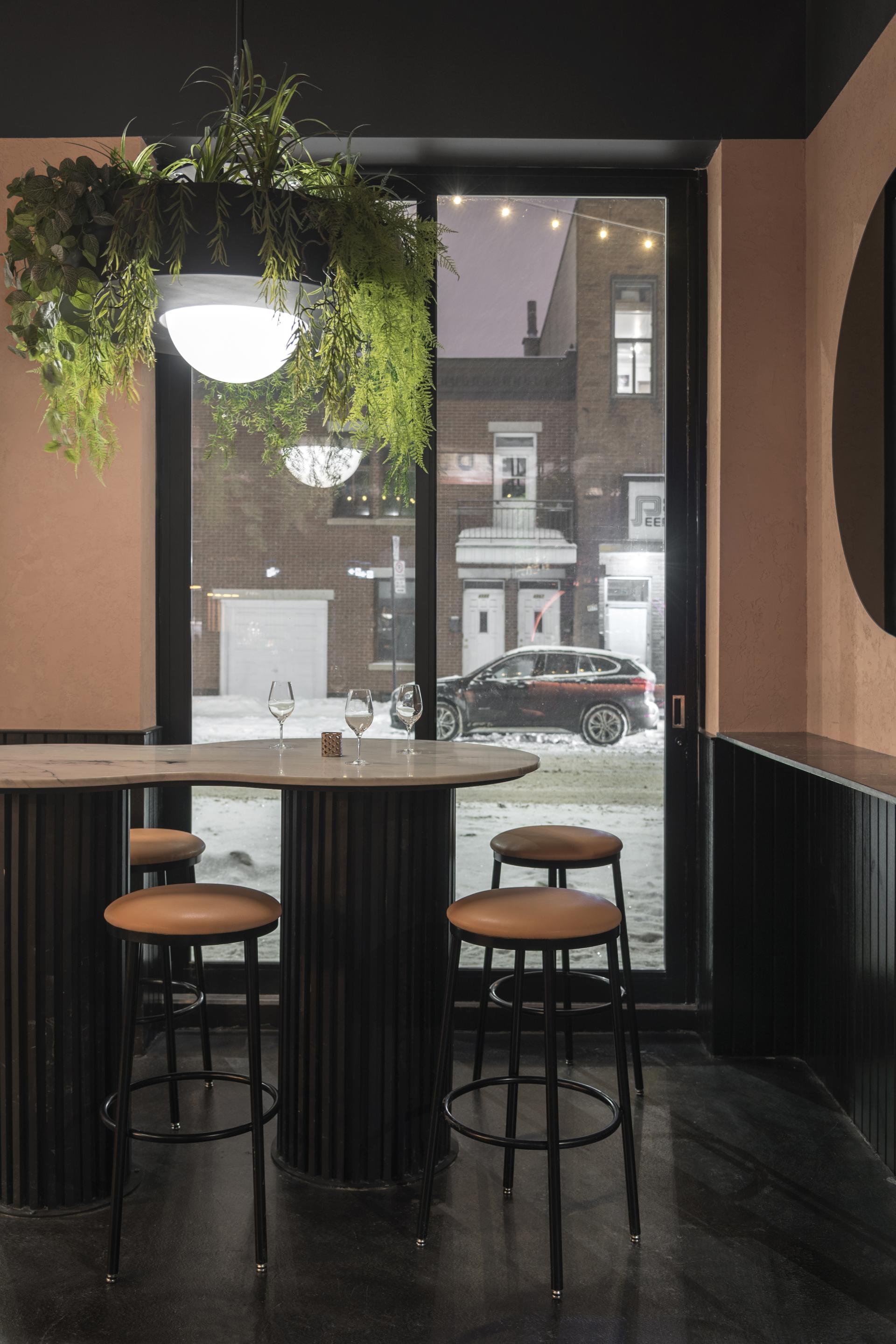 Tropical-themed restaurant interior with a marble-topped bar, plants, and winter scenery visible through large windows in Montreal.