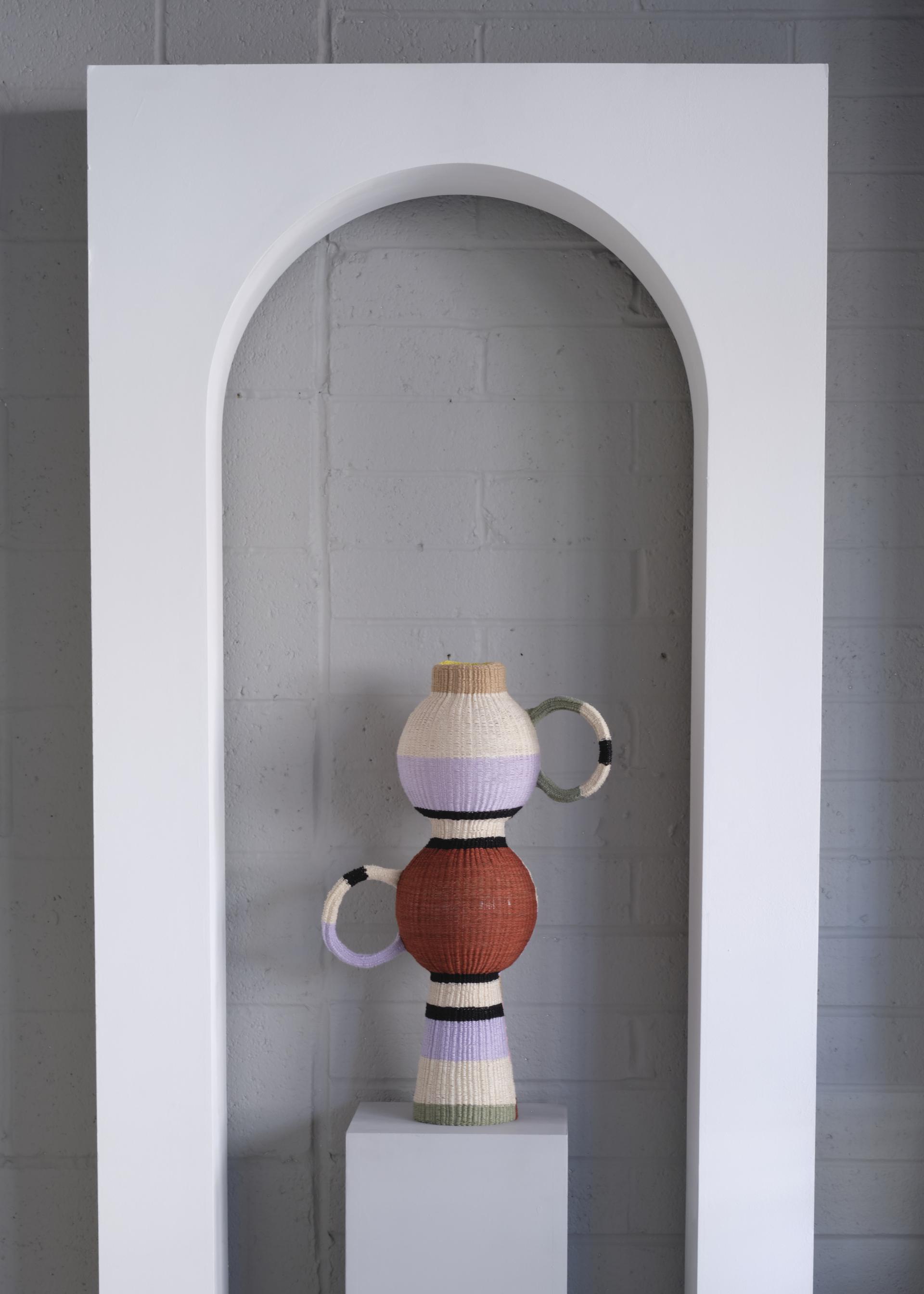 Colorful woven decorative vase displayed in a minimalist white arch, showcasing unique design from the London Design Festival.