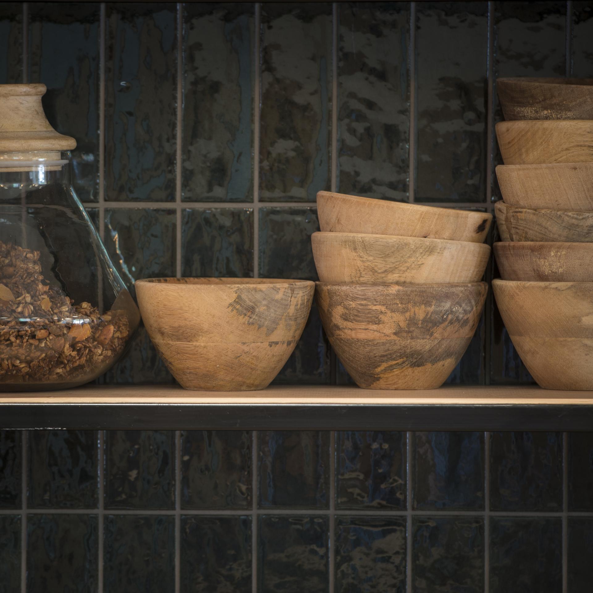 Wooden bowls arranged on a shelf, highlighting the natural textures, next to a glass jar filled with granola.