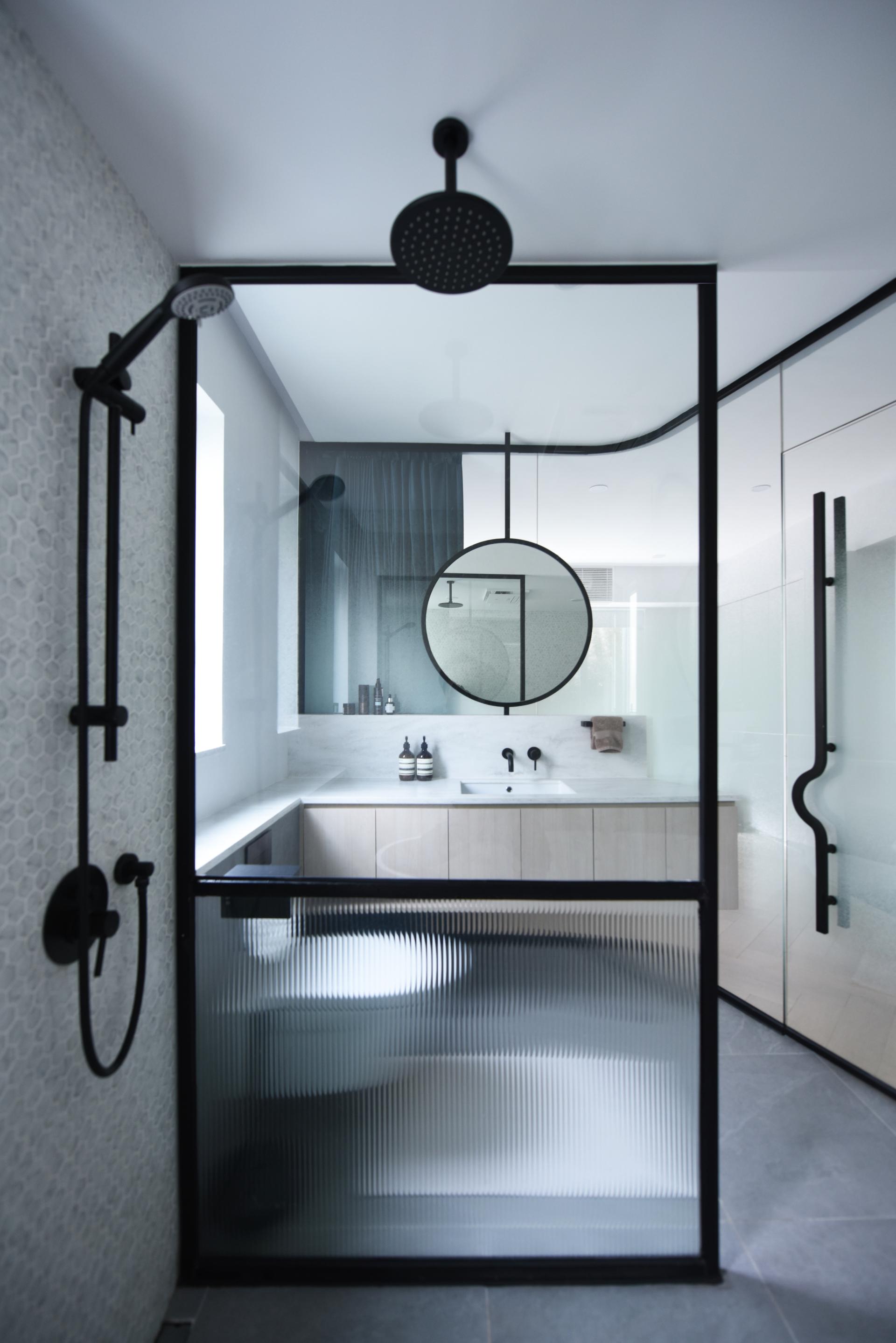 Modern bathroom design featuring a sleek glass shower enclosure, minimalist fixtures, and stylish circular mirror.