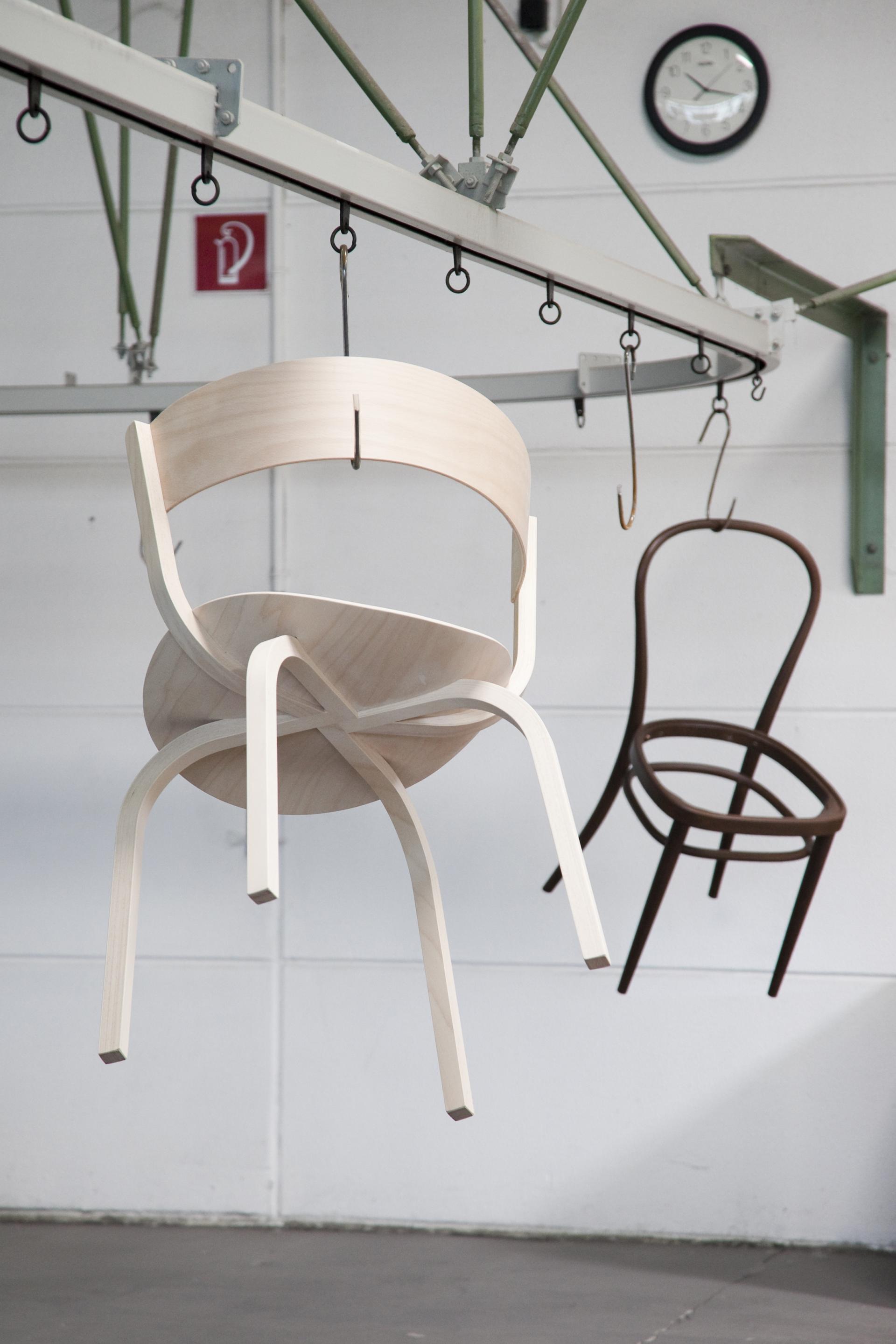 Two hanging chairs, one light wooden and one dark, showcased in a production facility, highlighting Thonet's craftsmanship.