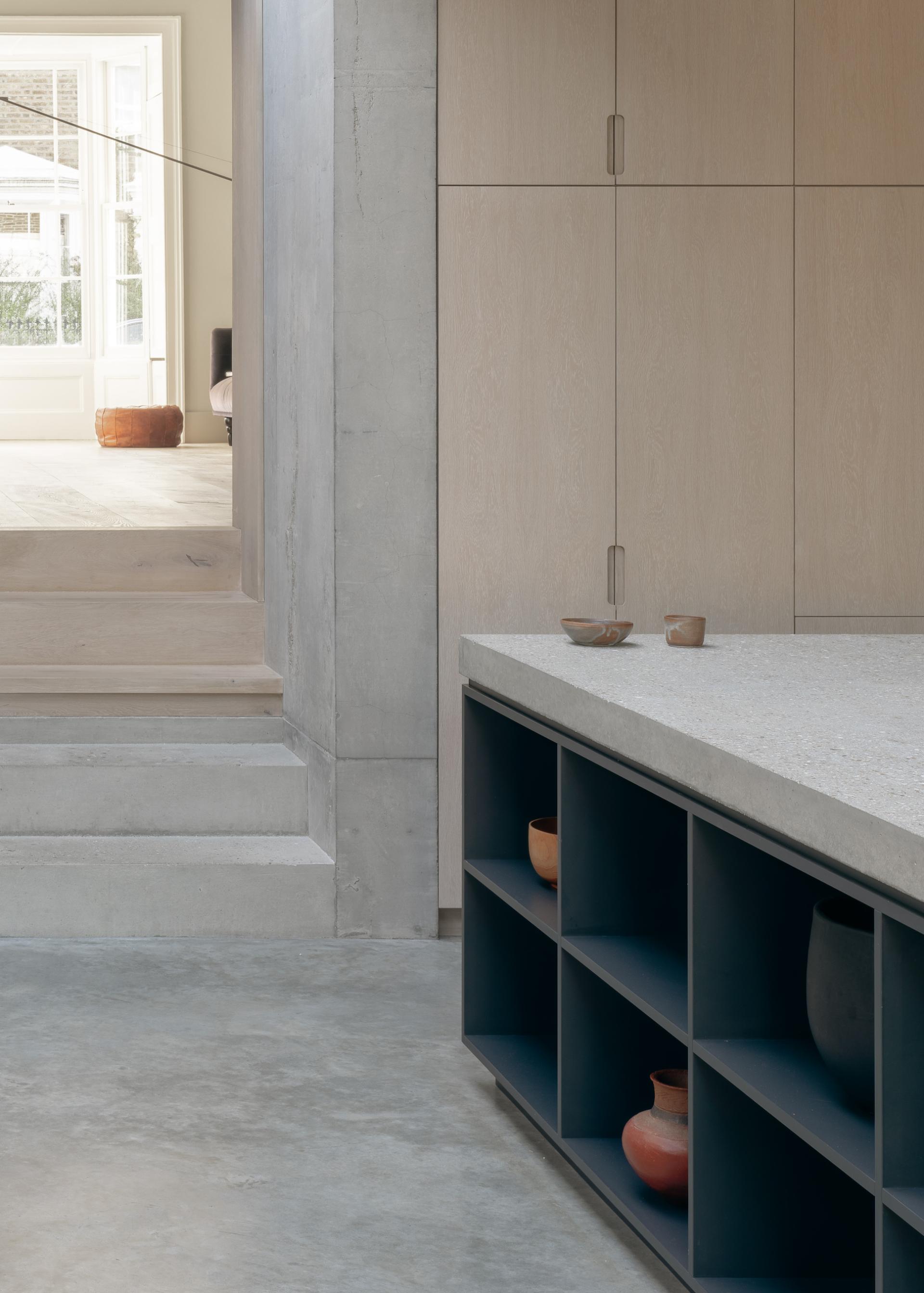 Modern interior featuring a concrete kitchen island, wooden cabinetry, and decorative pottery in the Concrete Plinth House by DGN Studio.