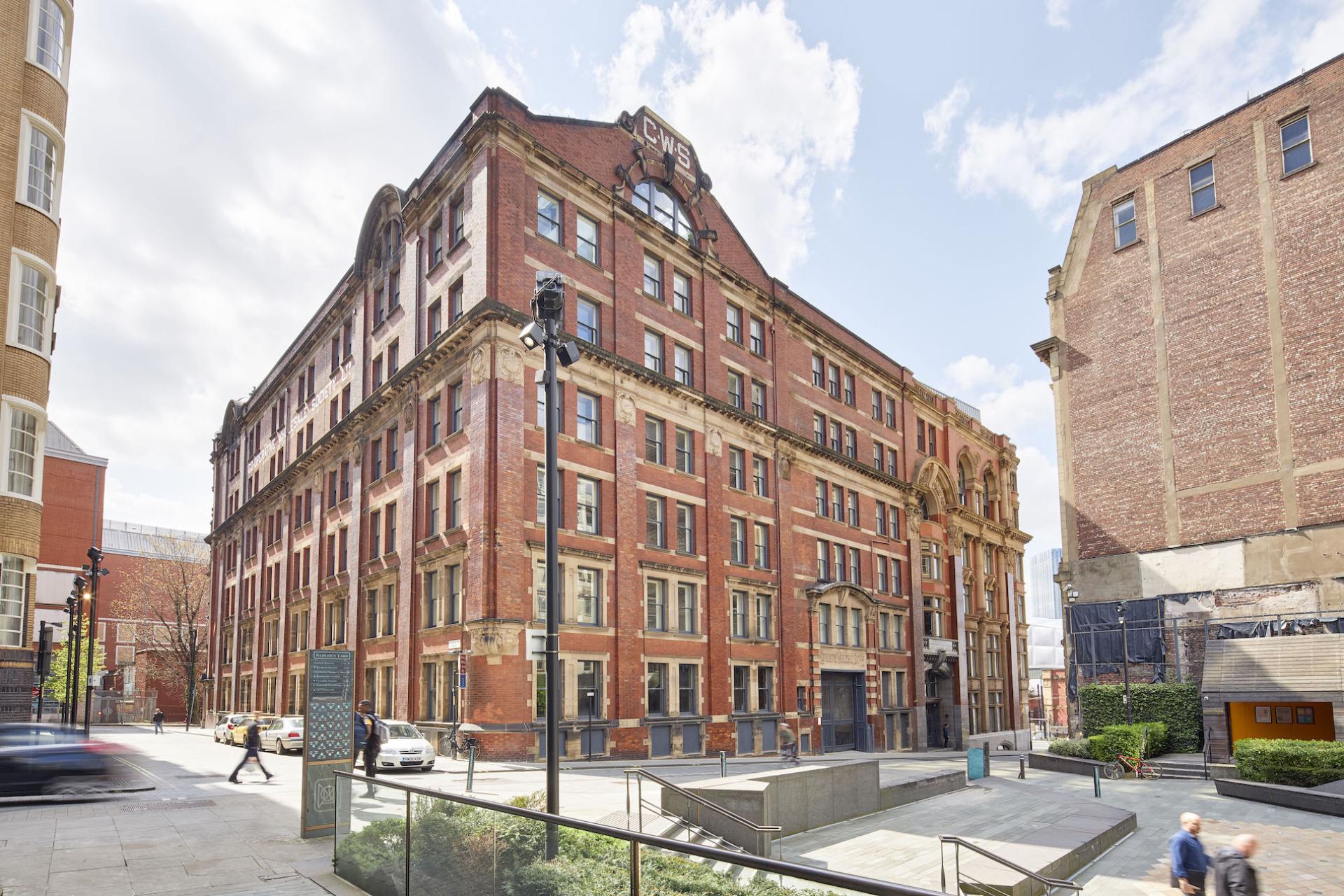 Historic red-brick building in Manchester, set to become the first Material Source Studio, surrounded by urban landscape.
