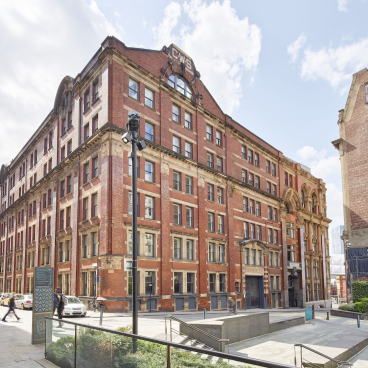 Historic red-brick building in Manchester, set to become the first Material Source Studio, surrounded by urban landscape.