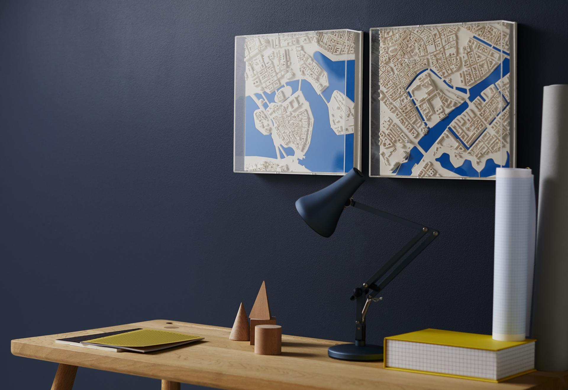 Three-dimensional city models displayed on a wall, showcasing urban landscapes alongside a modern workspace setup.