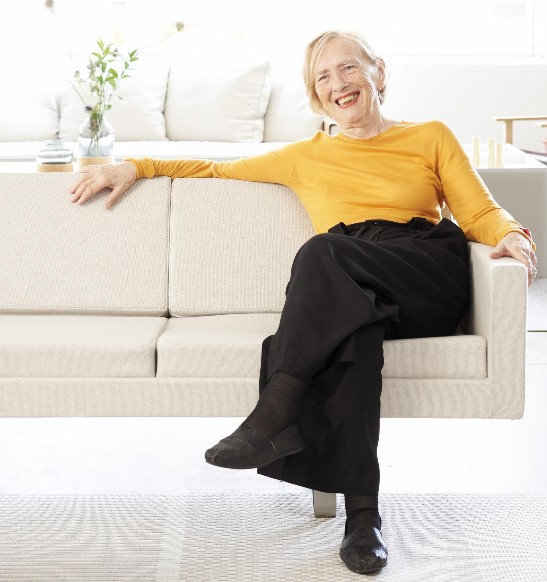 Bodil Kjær smiles while sitting elegantly on her architectural furniture, showcasing timeless Danish design.