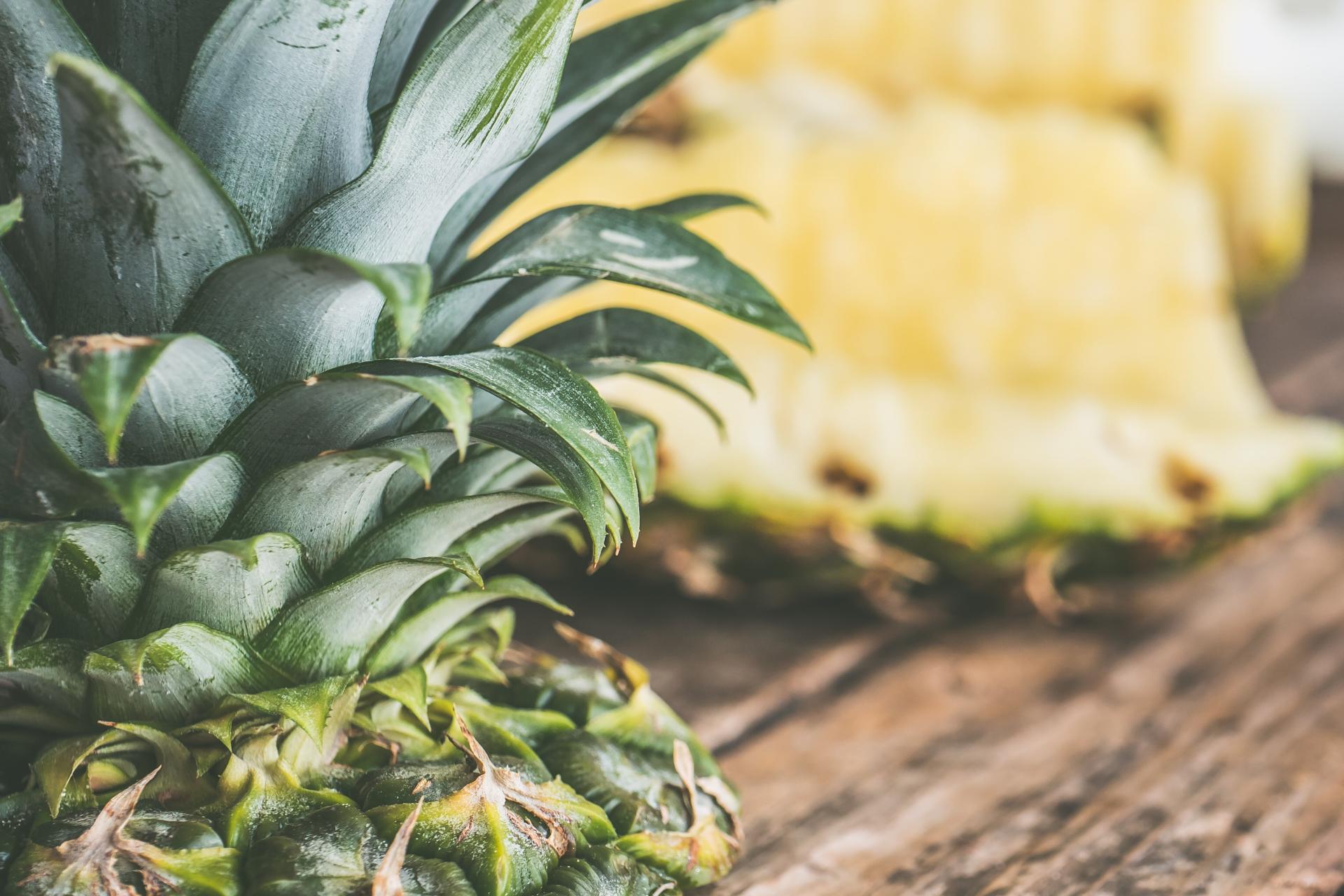 Fresh pineapple with green leaves, highlighted against sliced pineapple pieces on a wooden surface.