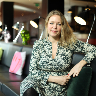 Melba Beetham, a designer and lecturer, poses in a stylish, modern interior space with cozy seating and lighting.