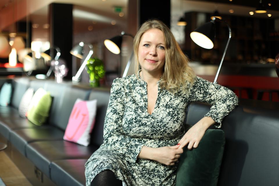 Melba Beetham, a designer and lecturer, poses in a stylish, modern interior space with cozy seating and lighting.