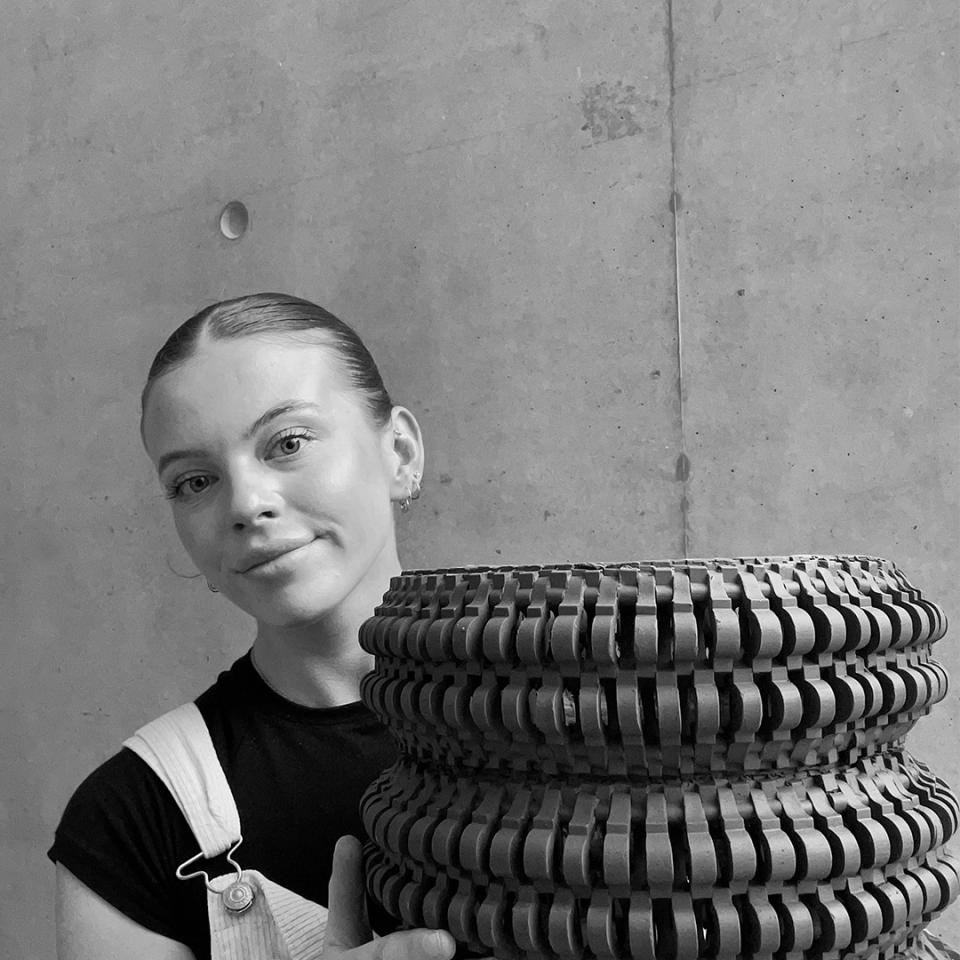 Textile designer Freyja Dorren poses with a unique woven creation against a minimalist concrete backdrop.