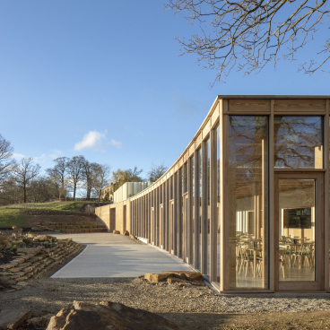 Modern visitor centre at Yorkshire Sculpture Park featuring large windows, wooden facade, and natural surroundings under a clear blue sky.