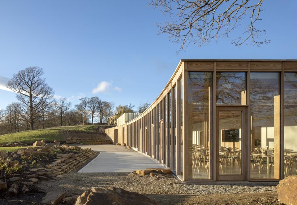 Modern visitor centre at Yorkshire Sculpture Park featuring large windows, wooden facade, and natural surroundings under a clear blue sky.